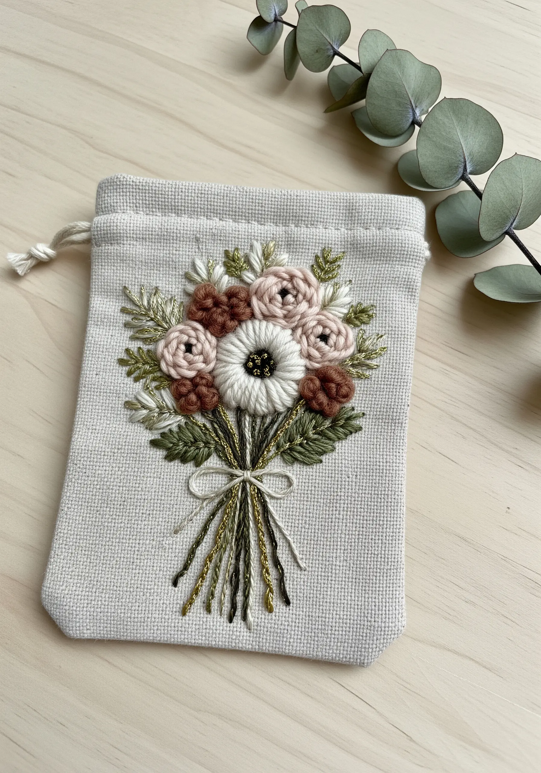 Dimensional floral bouquet with metallic thread accents embroidered on a small drawstring bag.