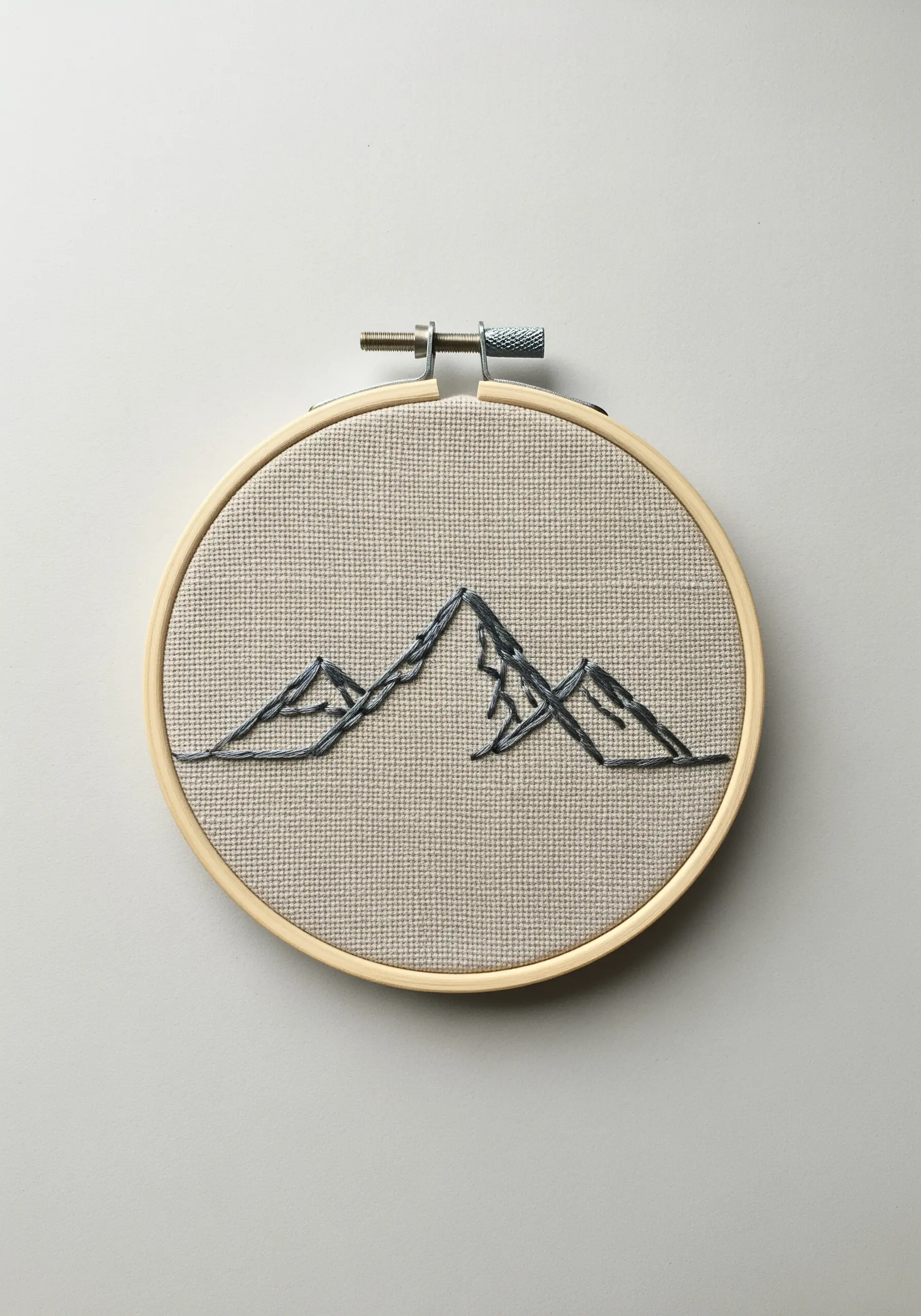 Minimalist mountain range embroidered with gray thread using varied backstitch on linen fabric in a hoop.