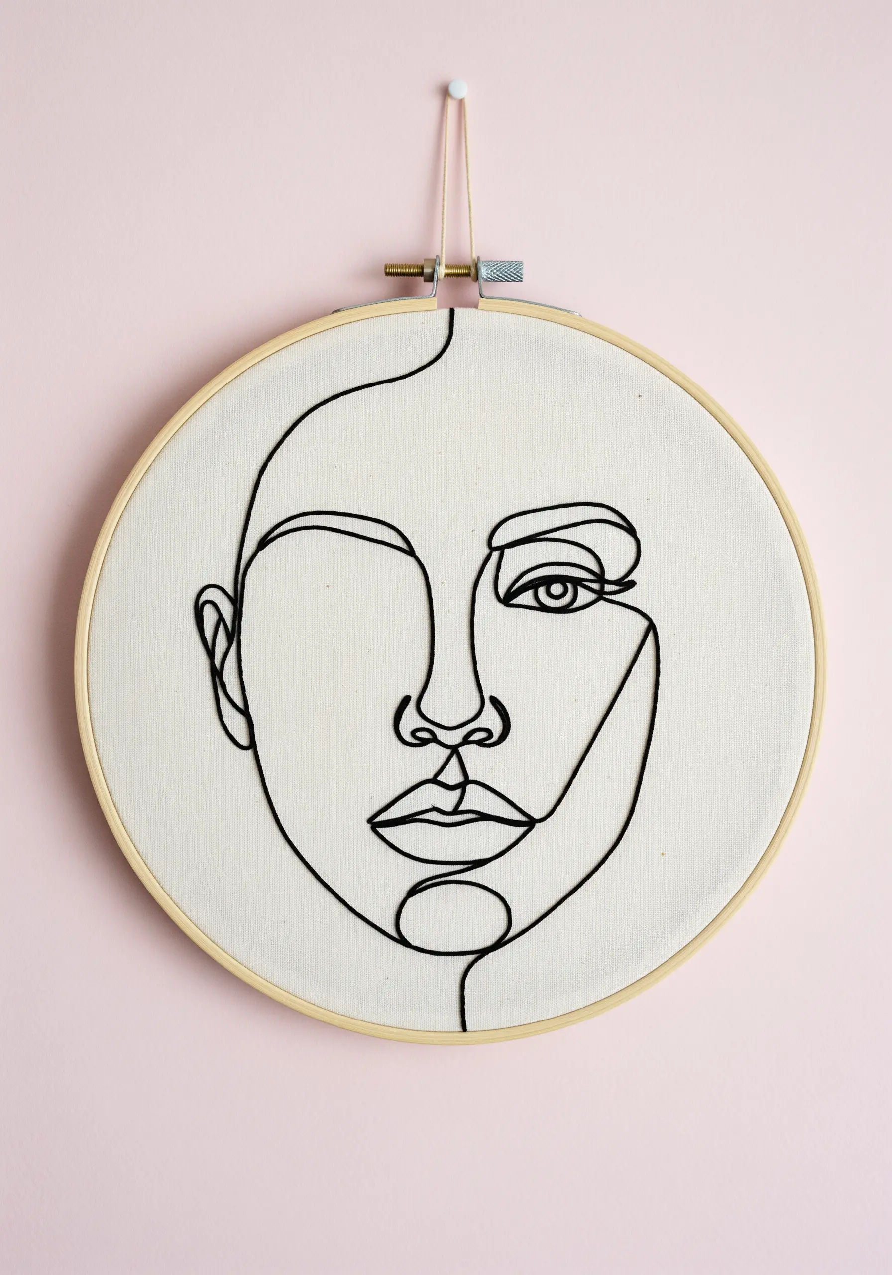 A minimalist one-line portrait embroidered in black thread using a whipped stem stitch.