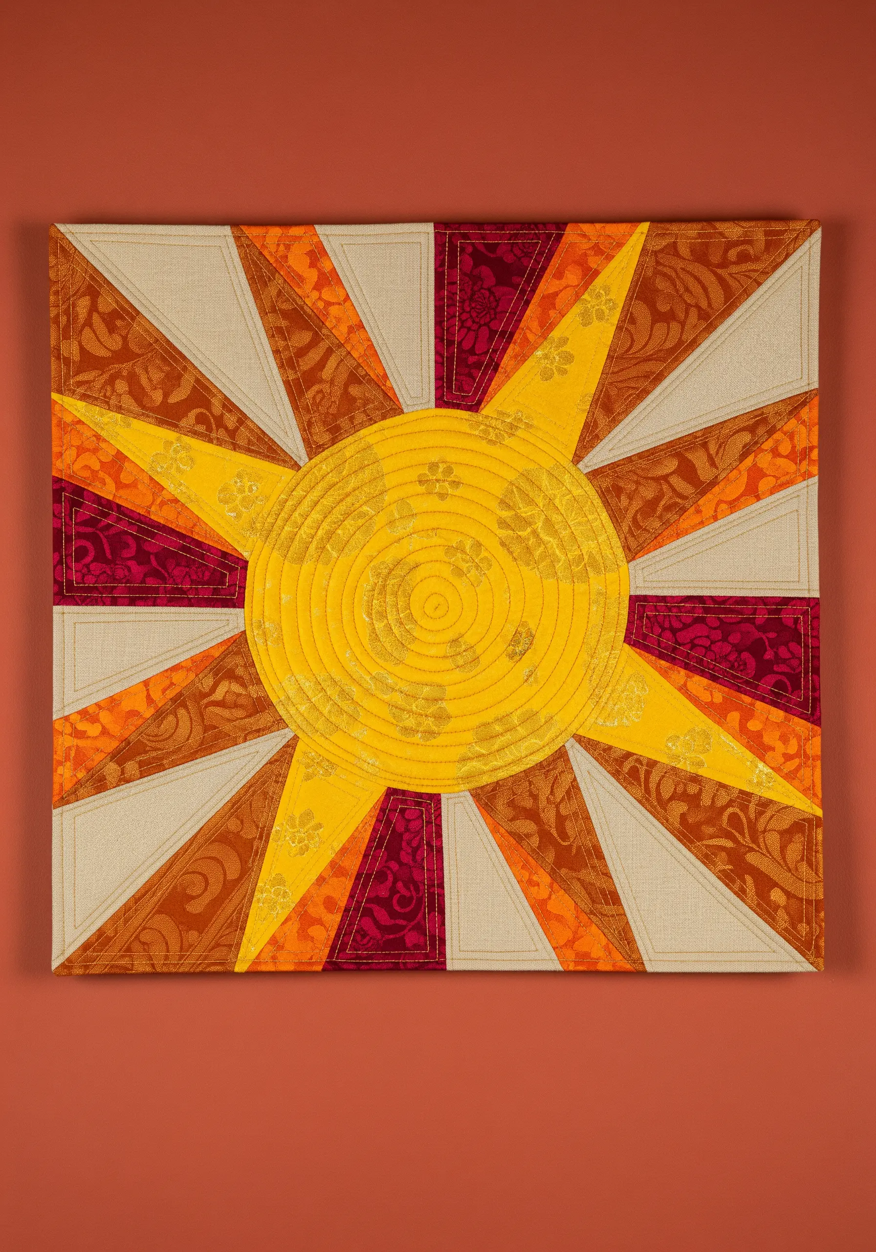 A quilted sun design with radiating rays made from yellow, orange, and red patterned fabrics.