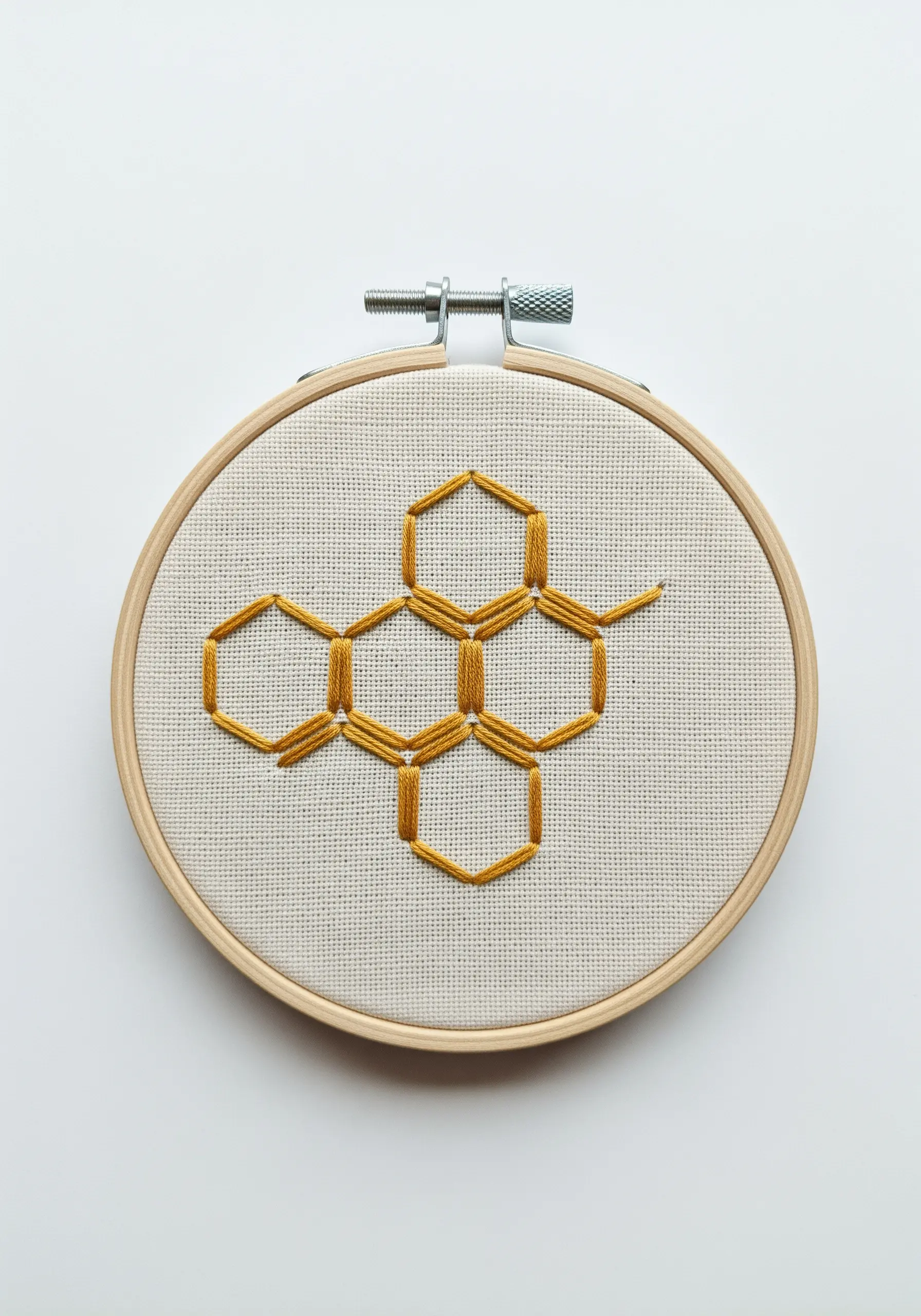 A geometric honeycomb pattern embroidered with golden-yellow satin stitch in a hoop.