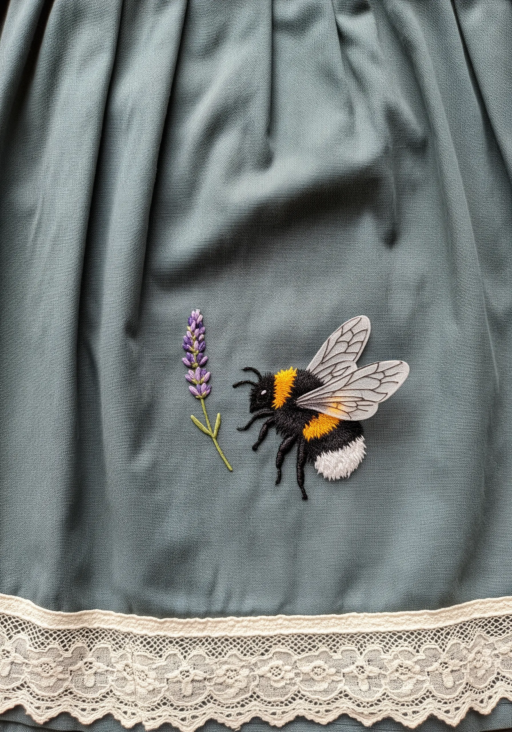 A realistic embroidered bumblebee with sheer appliqué wings next to a sprig of lavender.
