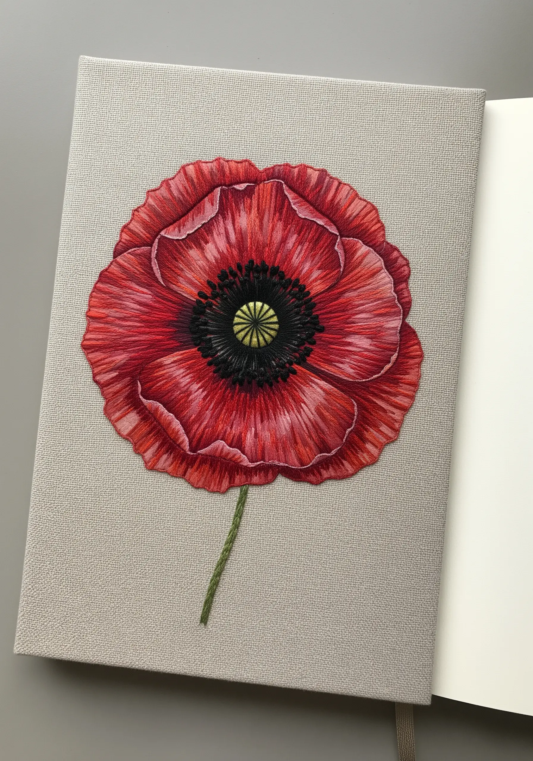 A realistic red poppy with detailed thread painting on the cover of a fabric notebook.