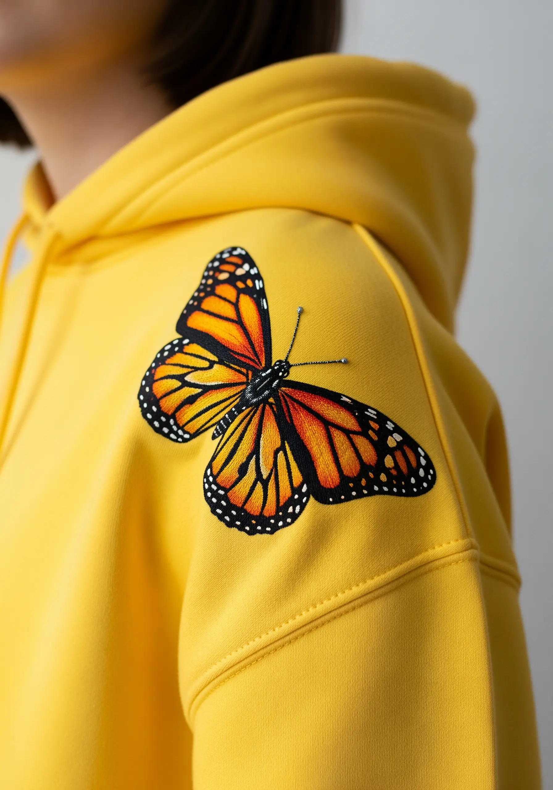 A vibrant monarch butterfly with detailed orange and black wings on a yellow hoodie's shoulder.