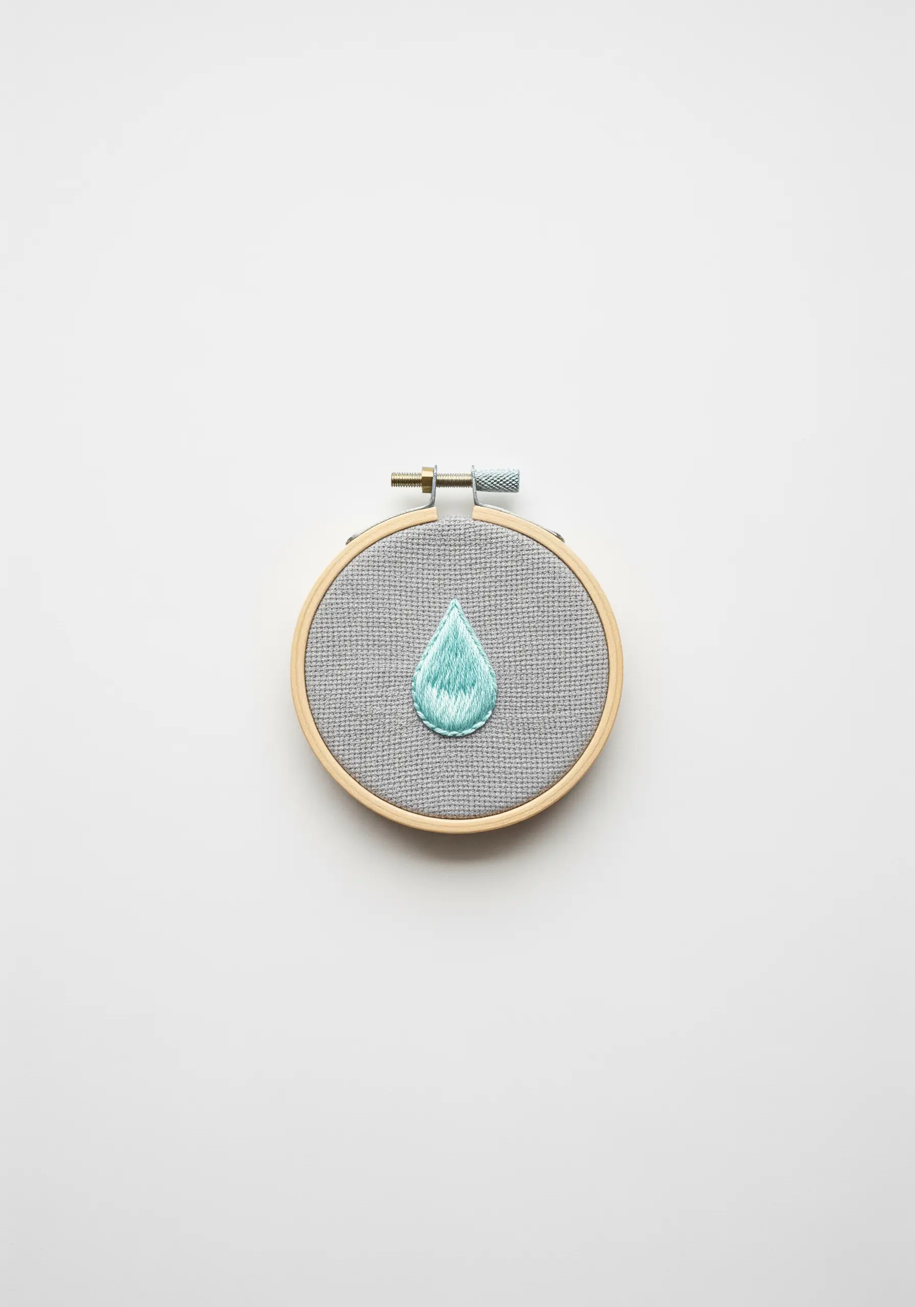 An embroidered raindrop with a color gradient on gray fabric.