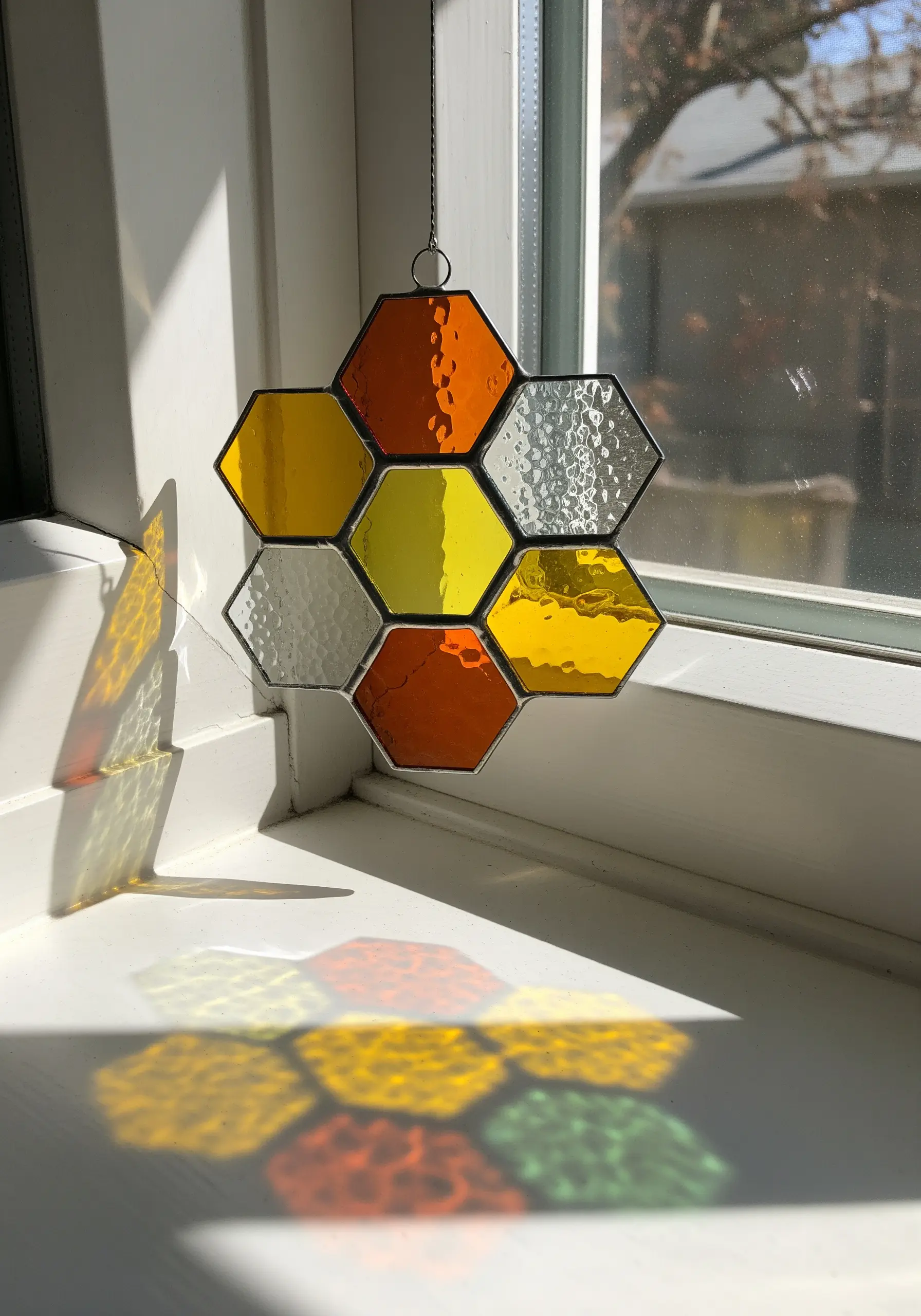 A honeycomb-patterned stained glass suncatcher with yellow and orange glass in a window.