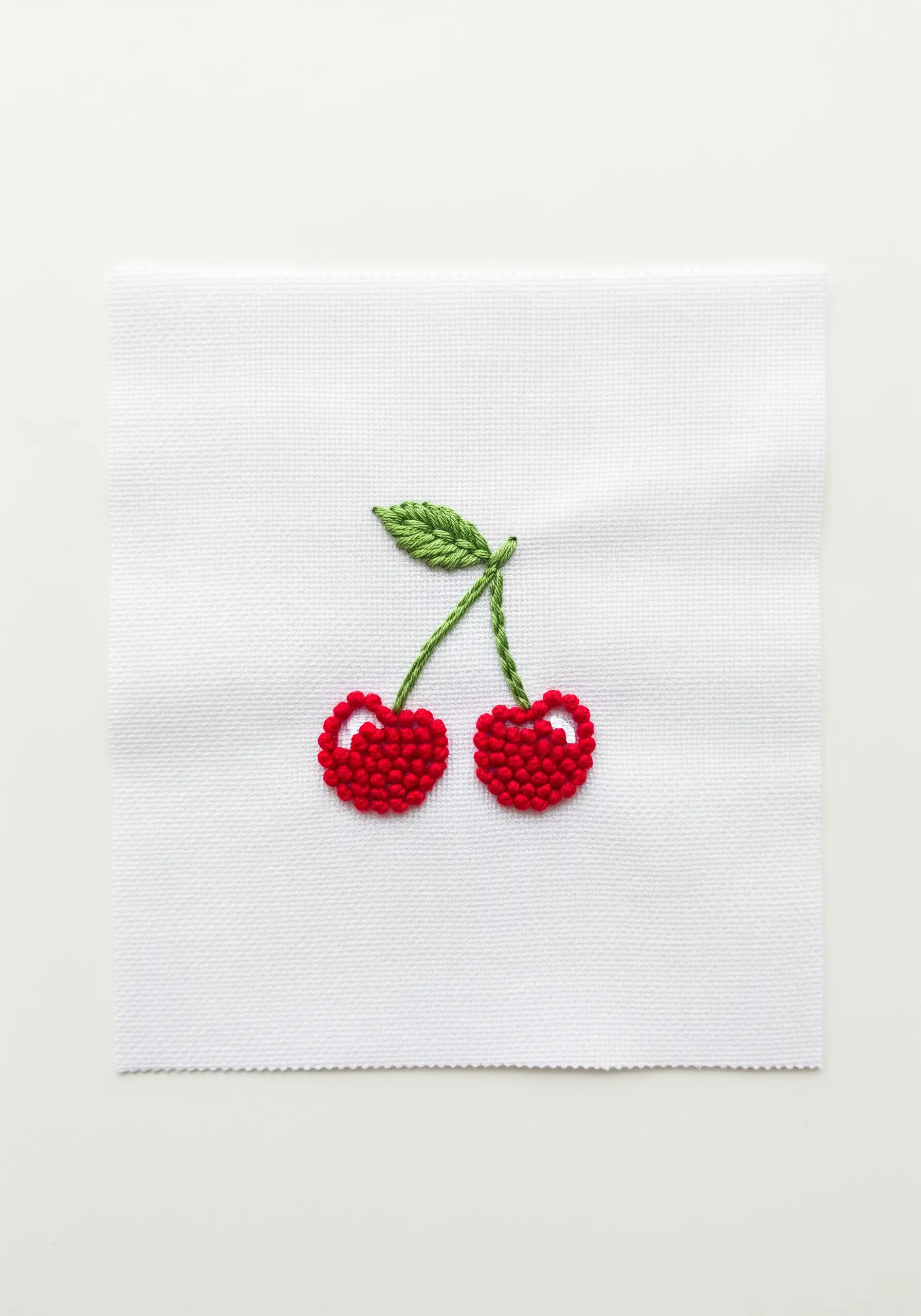 A pair of cherries embroidered with textured red French knots and a green leaf.