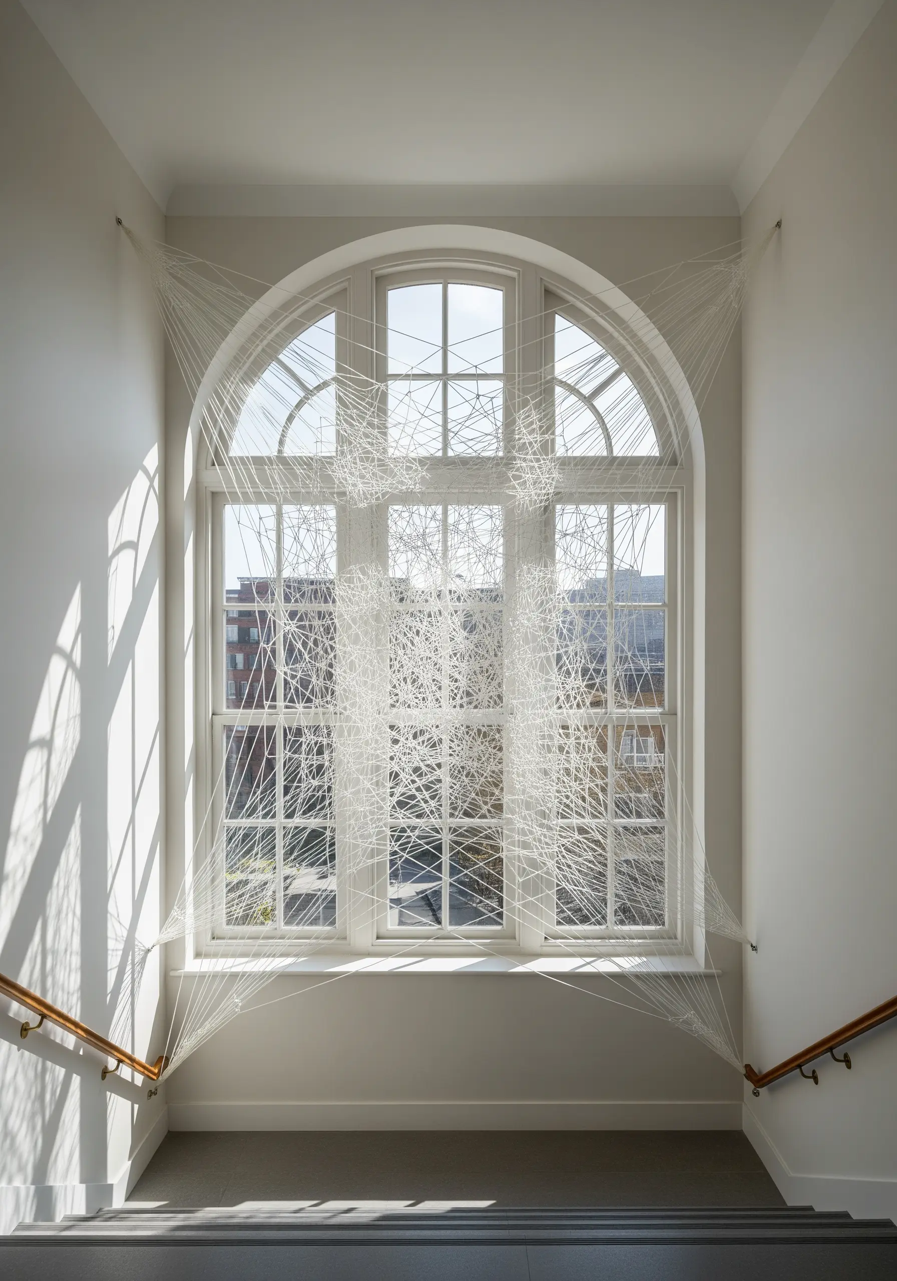 An abstract installation of white string stretched across an arched window, creating a web-like effect.