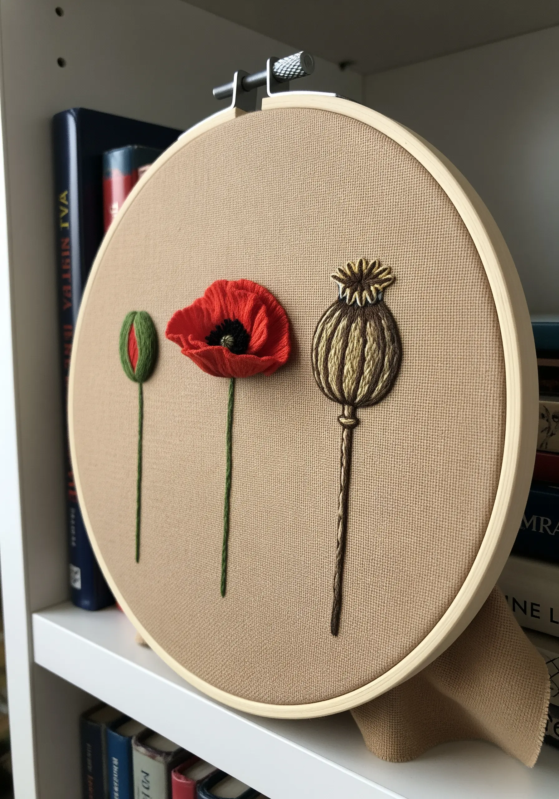 Minimalist embroidery showing the life cycle of a poppy, with one 3D stumpwork petal.