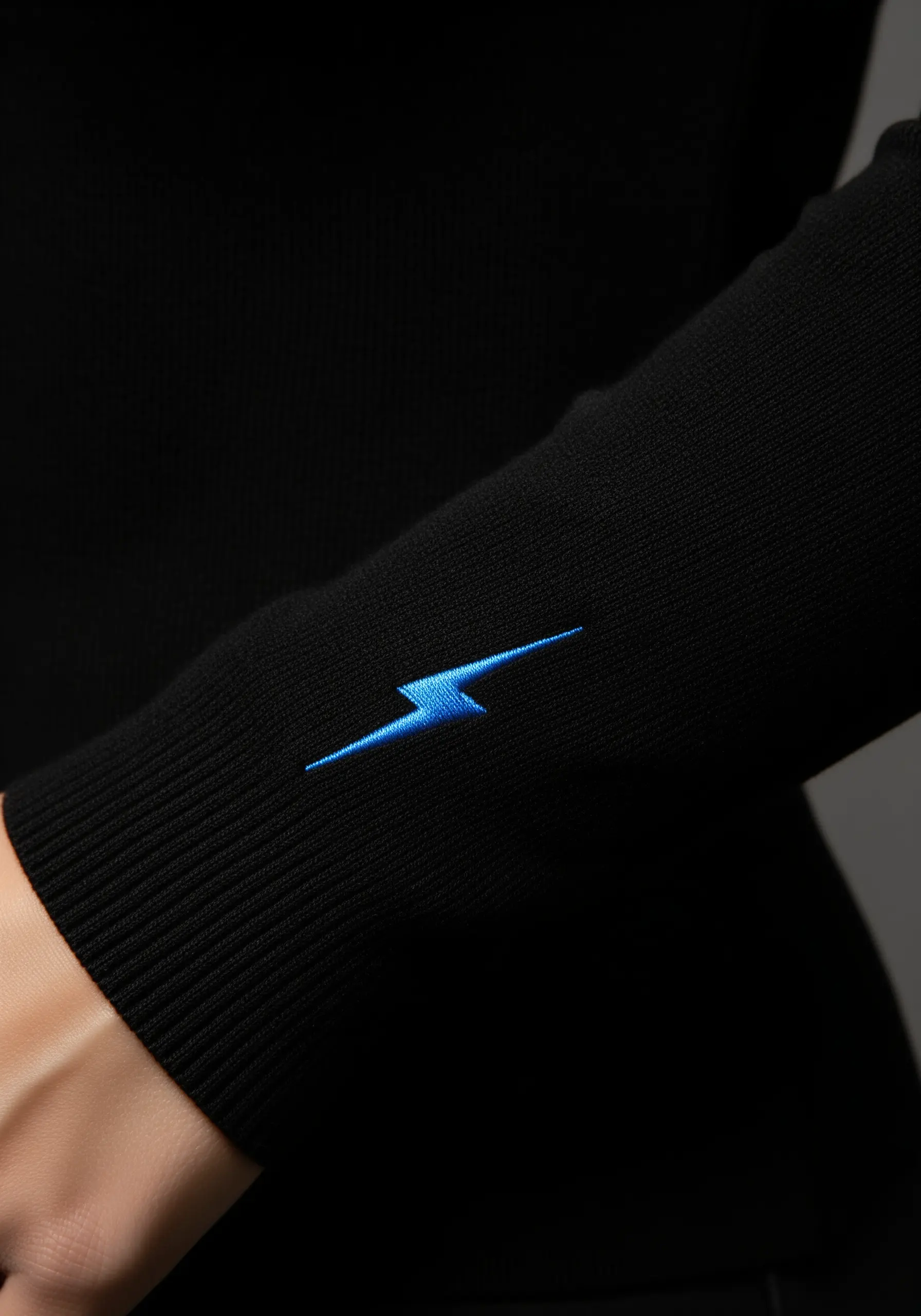 A small, bright blue lightning bolt embroidered on the black cuff of a sweater sleeve.