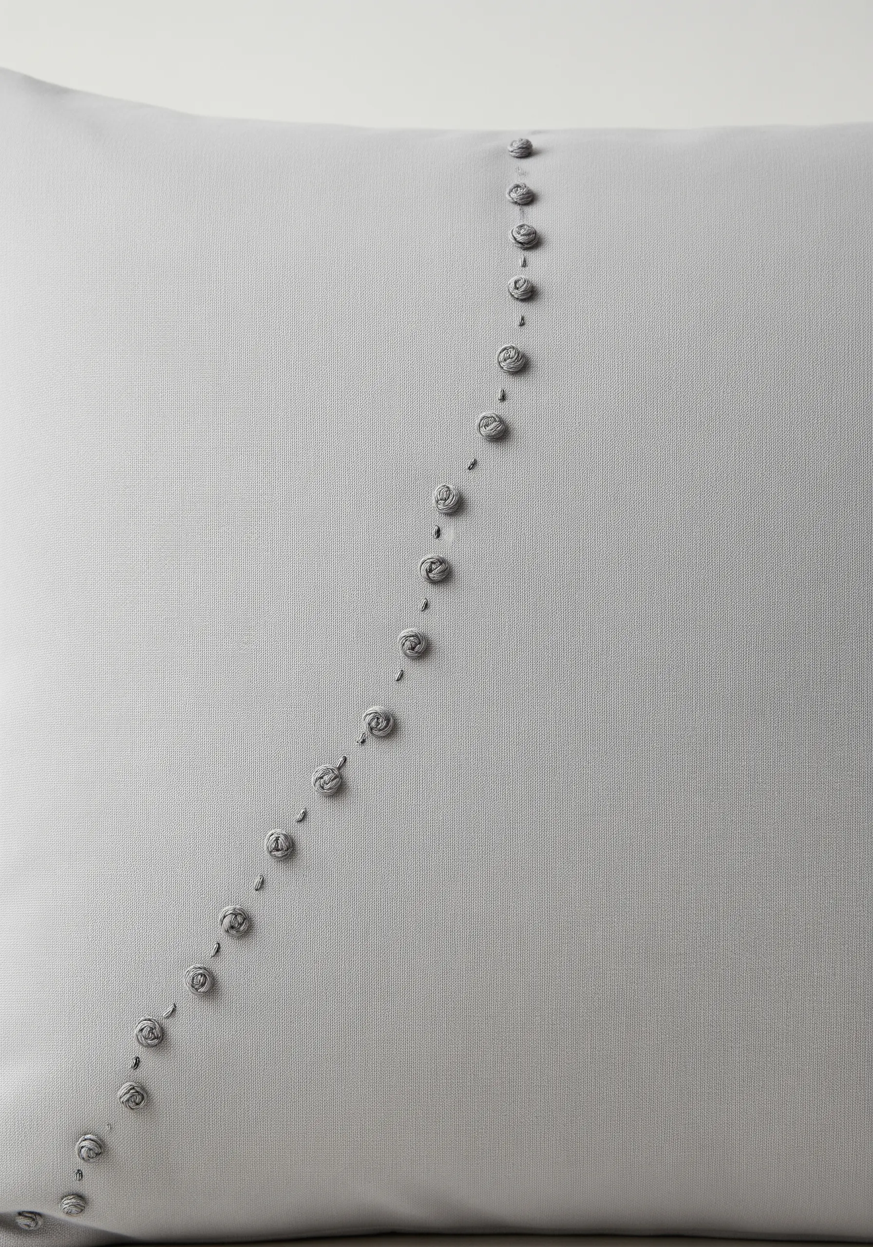 A diagonal line of small, gray, textured bullion knots on a light gray pillowcase.