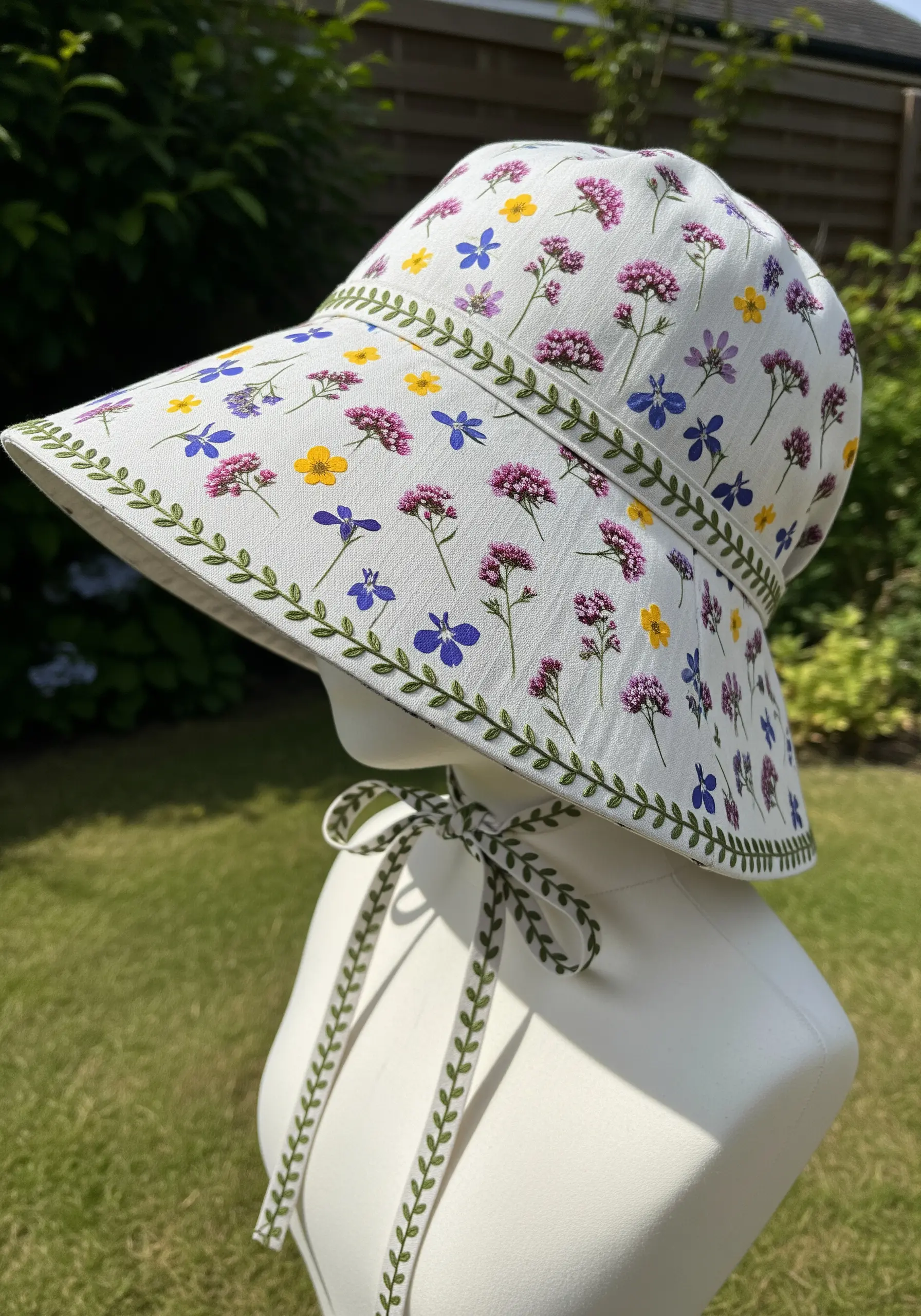 A white sun hat with a floral print, enhanced with an embroidered green vine border.