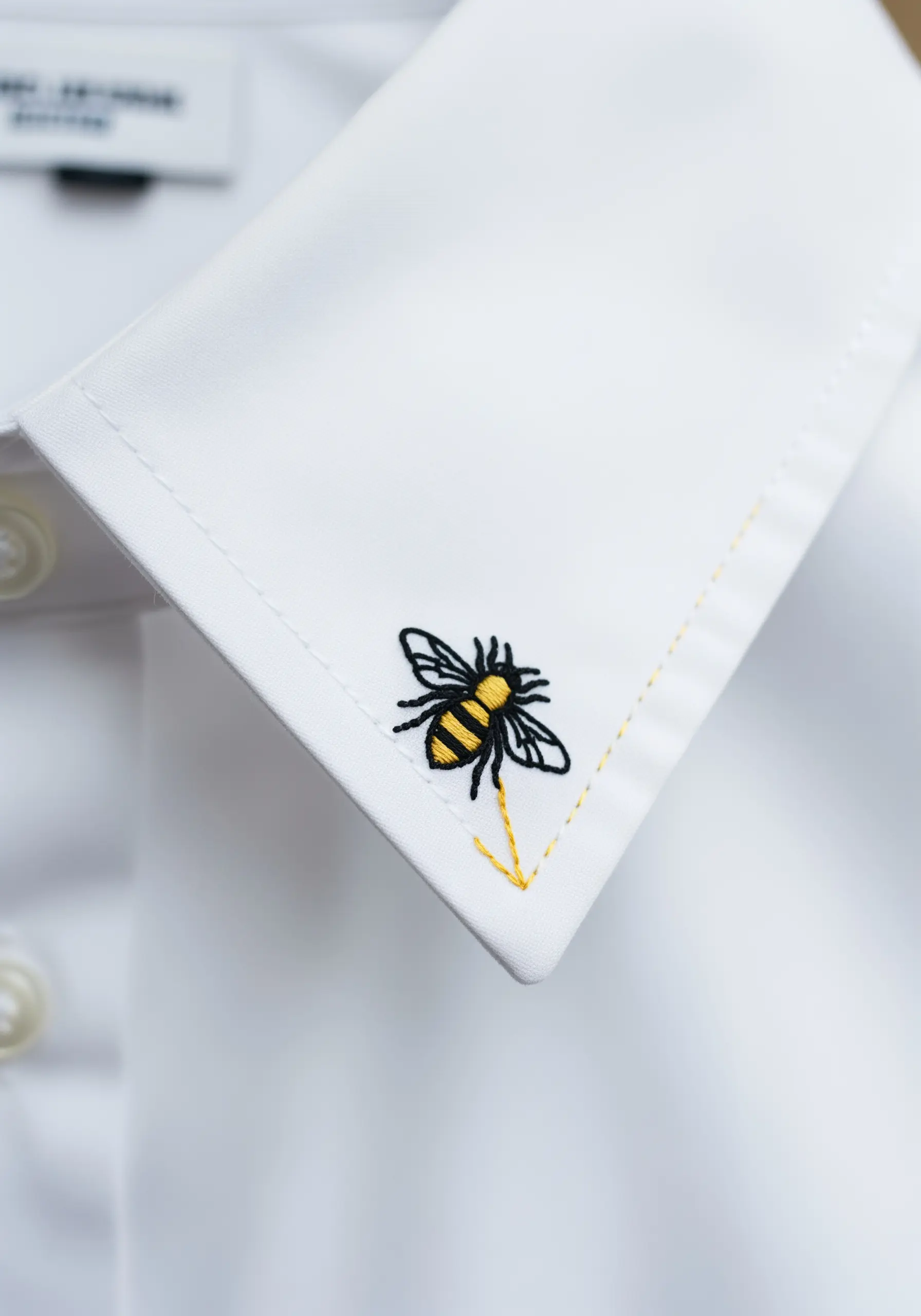 A small, detailed bee embroidered on the corner of a crisp white shirt cuff.