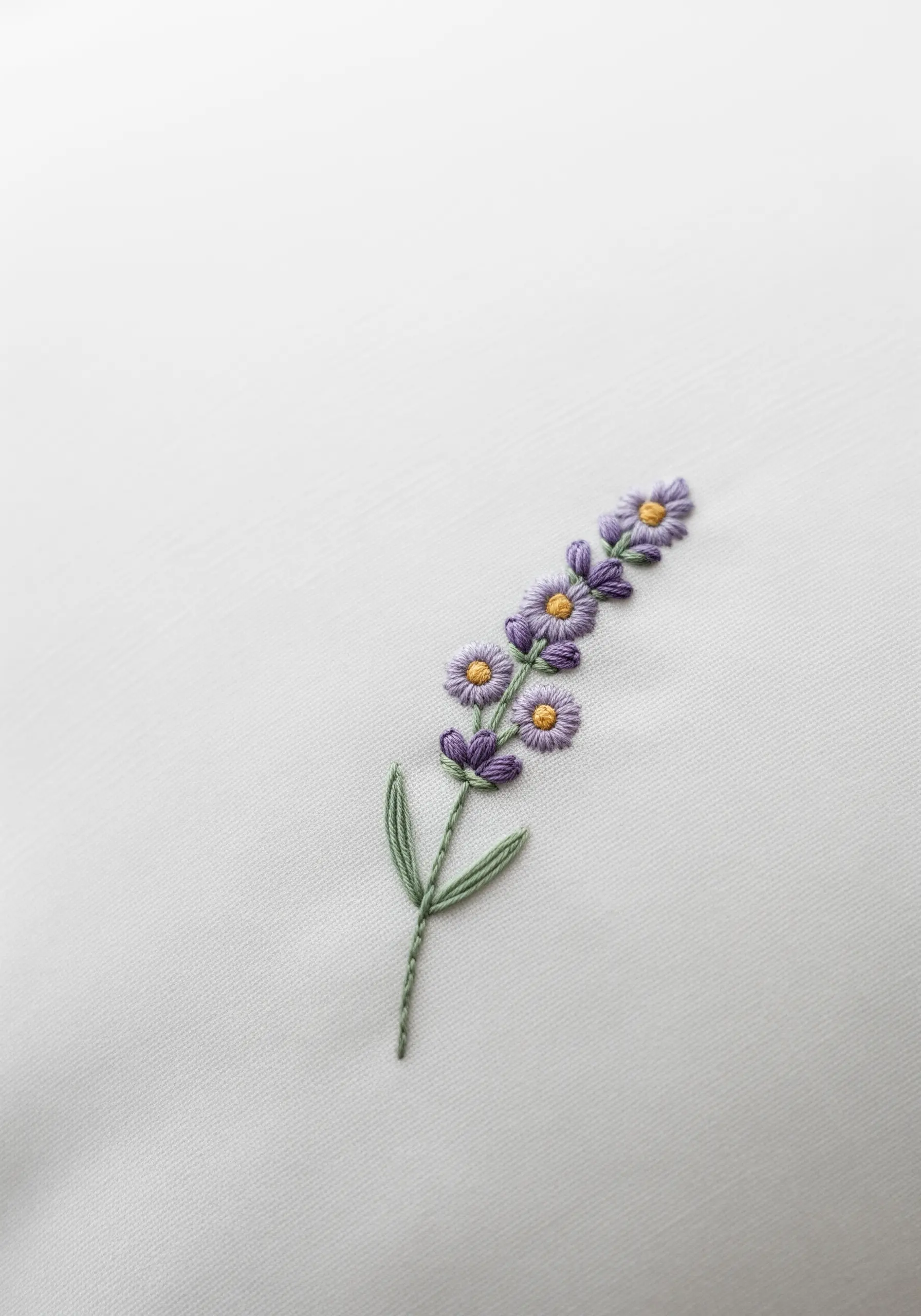 A single sprig of lavender embroidered with purple, yellow, and green thread on a white pillowcase.