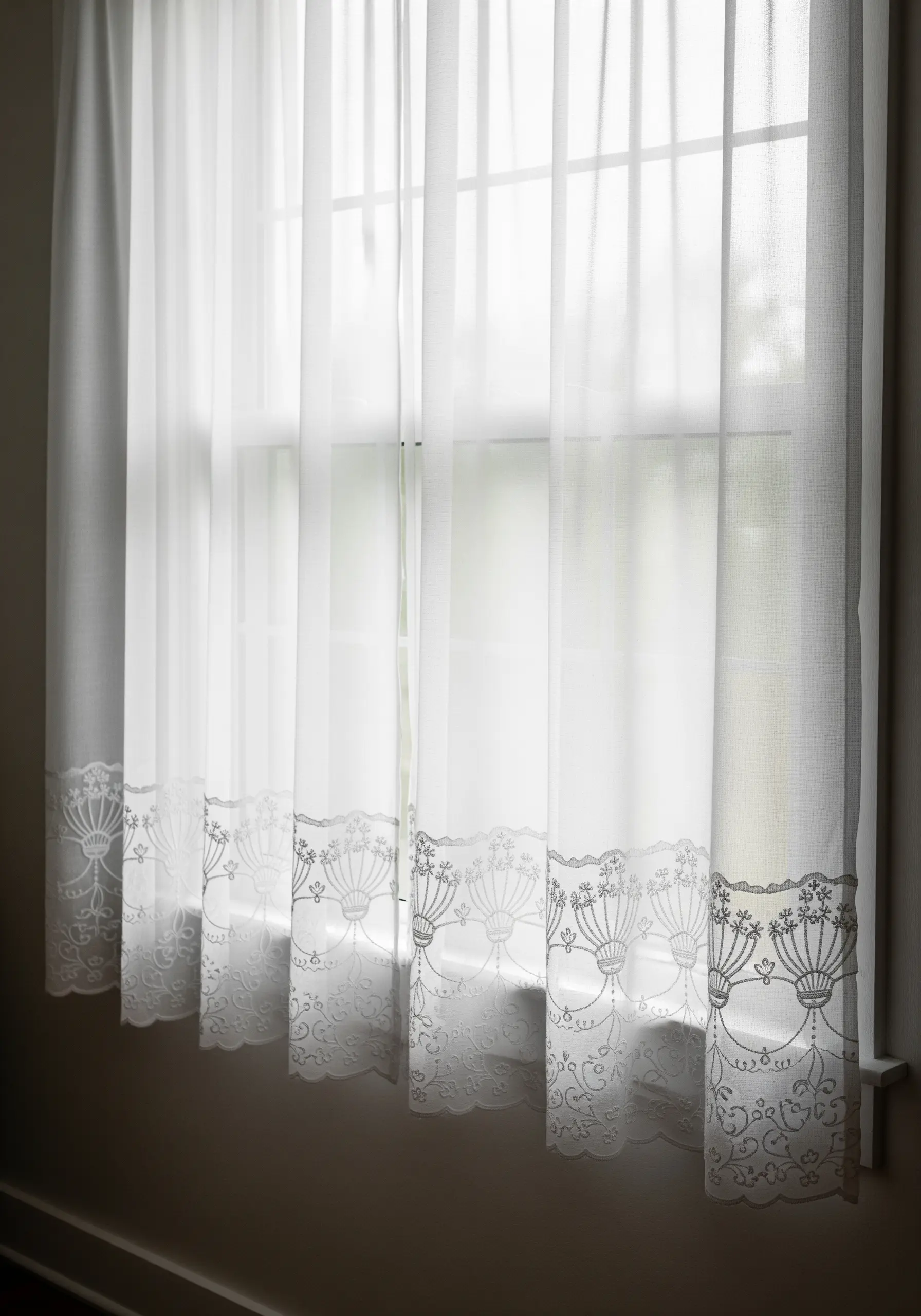 White sheer curtains with an elegant, repeating floral border embroidered in white thread.