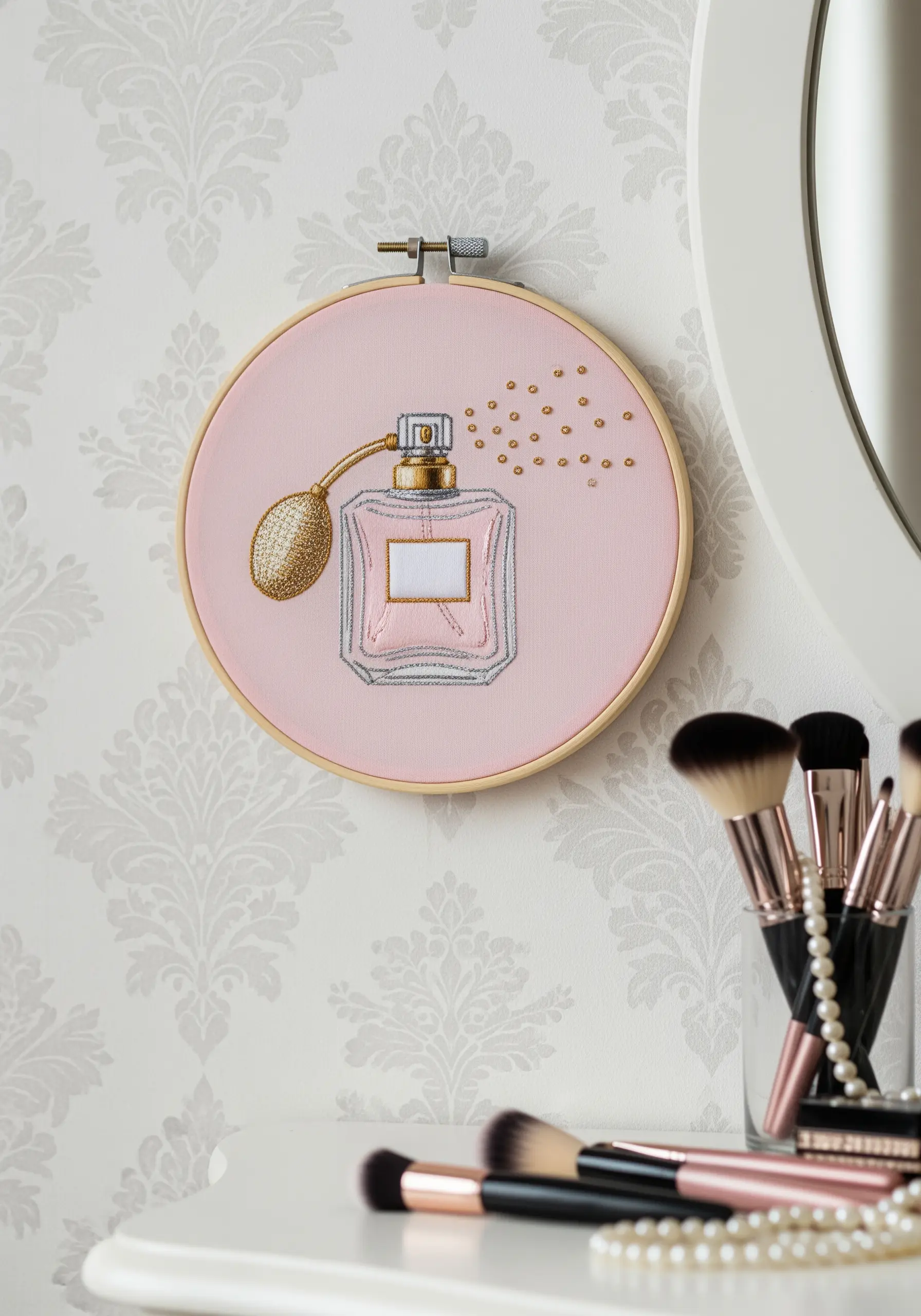 Embroidery of a vintage perfume bottle with gold metallic thread accents on pink fabric.