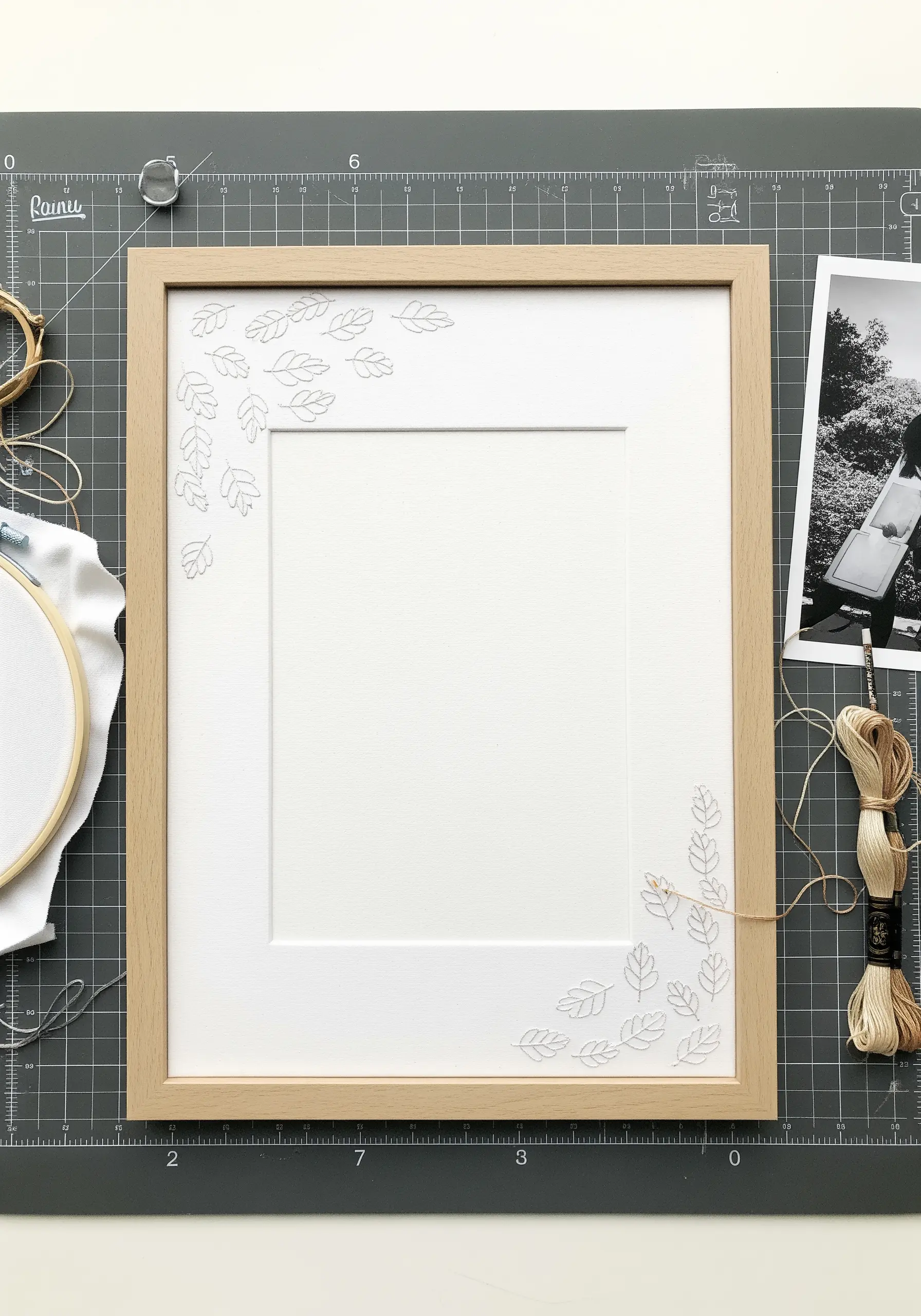 A wooden picture frame with tiny leaves hand-embroidered directly onto the white mat board.