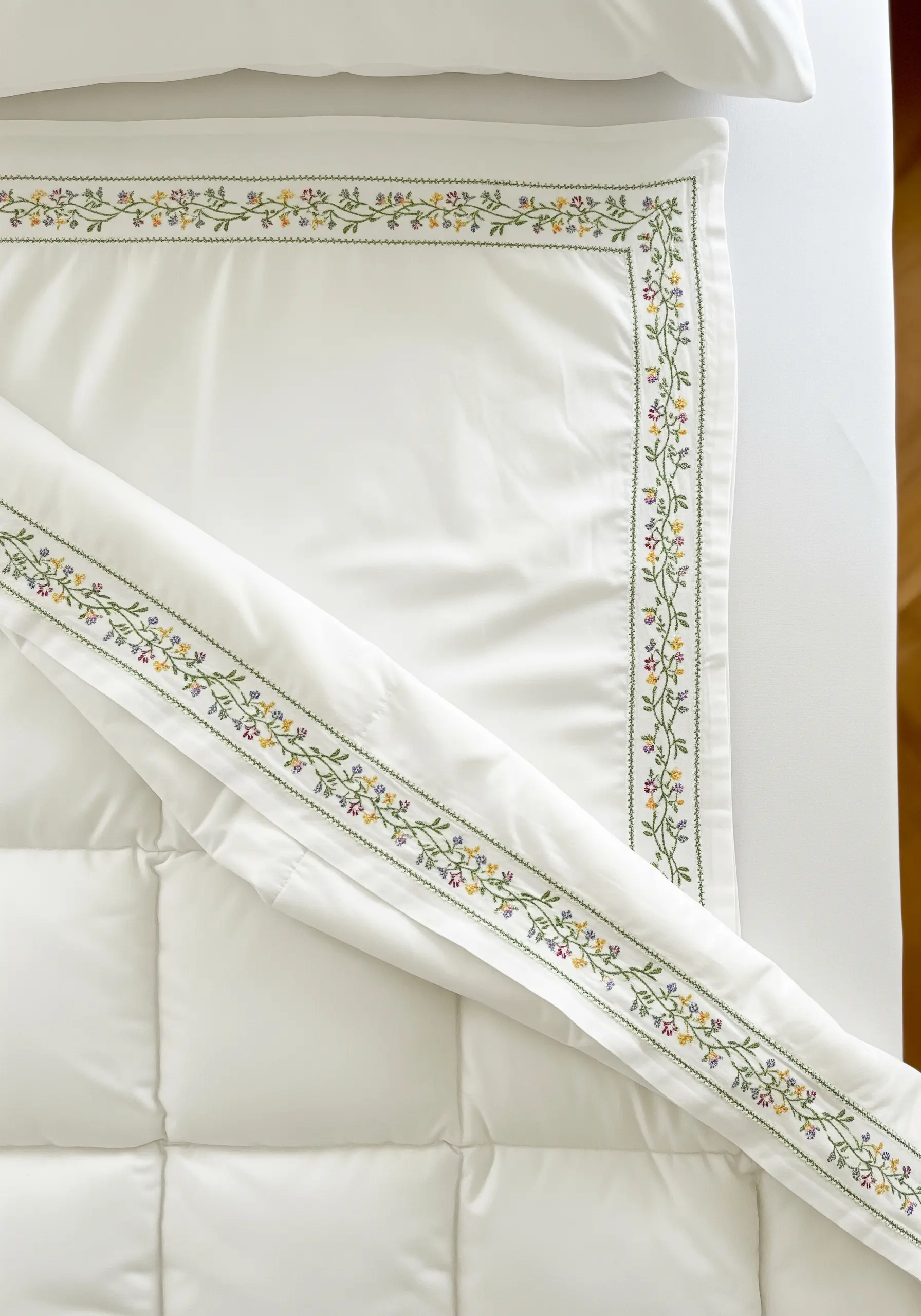 A delicate, colorful floral vine embroidered as a thin border on a white duvet cover.