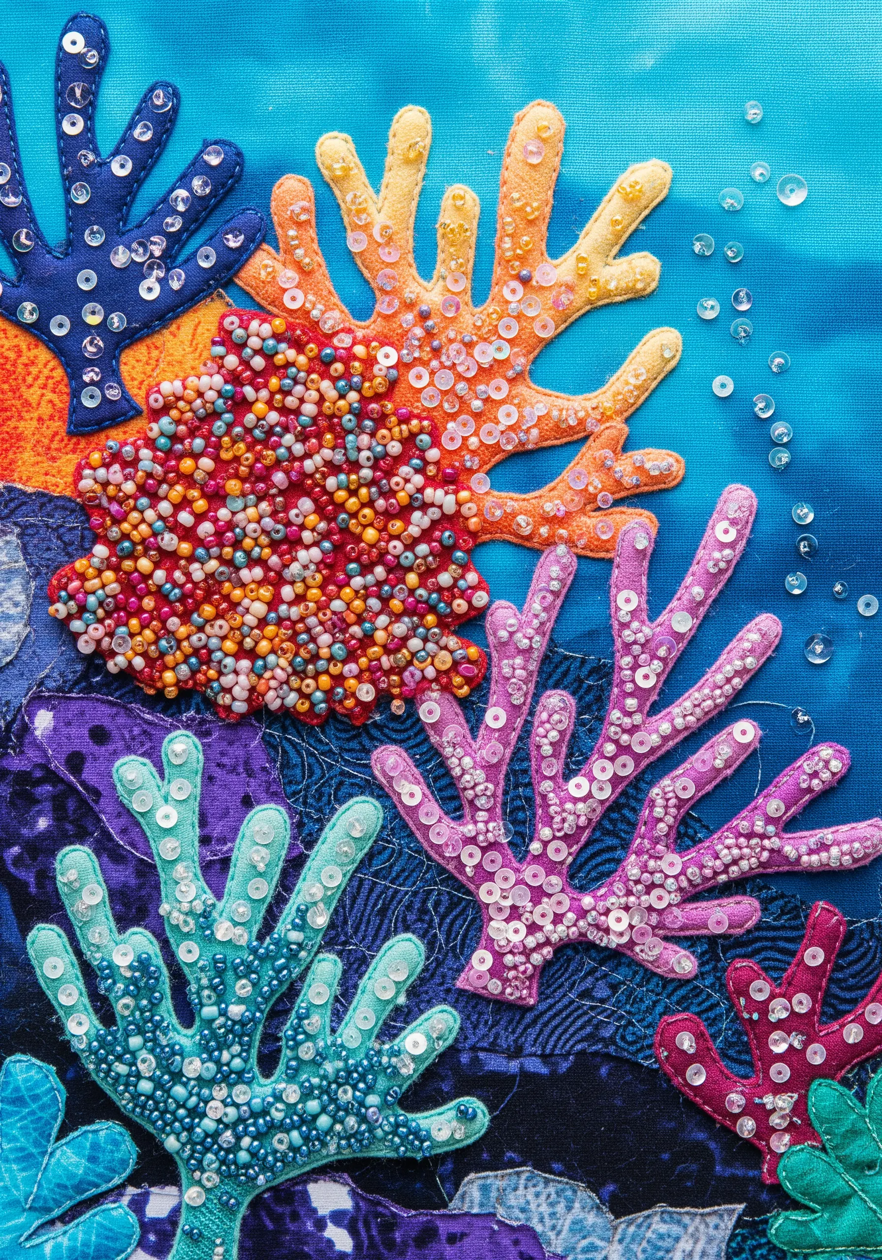Fabric collage of coral embellished with dense clusters of colorful beads and sequins.