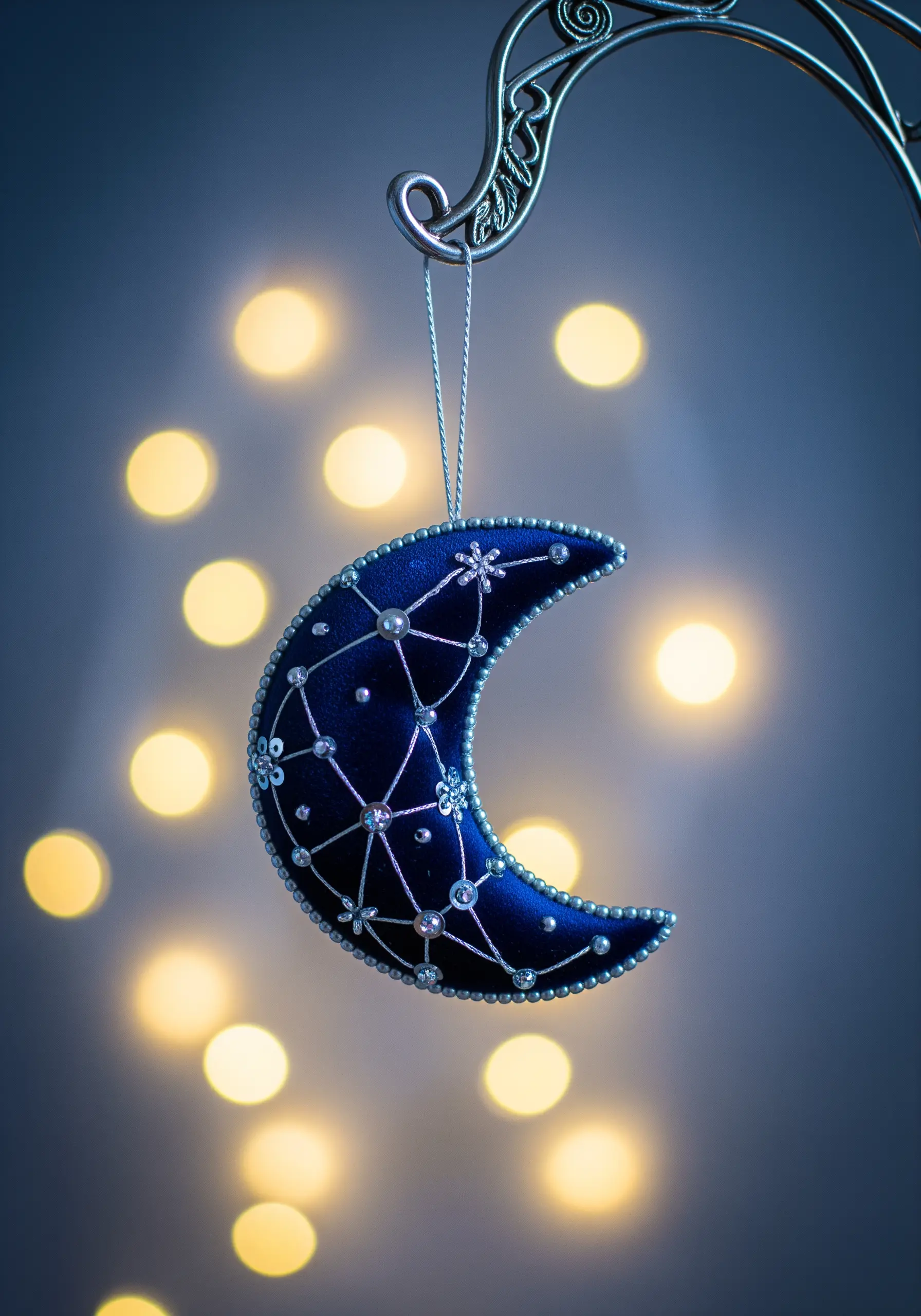 A padded, crescent moon ornament made of dark blue satin and decorated with silver beads and sequins.