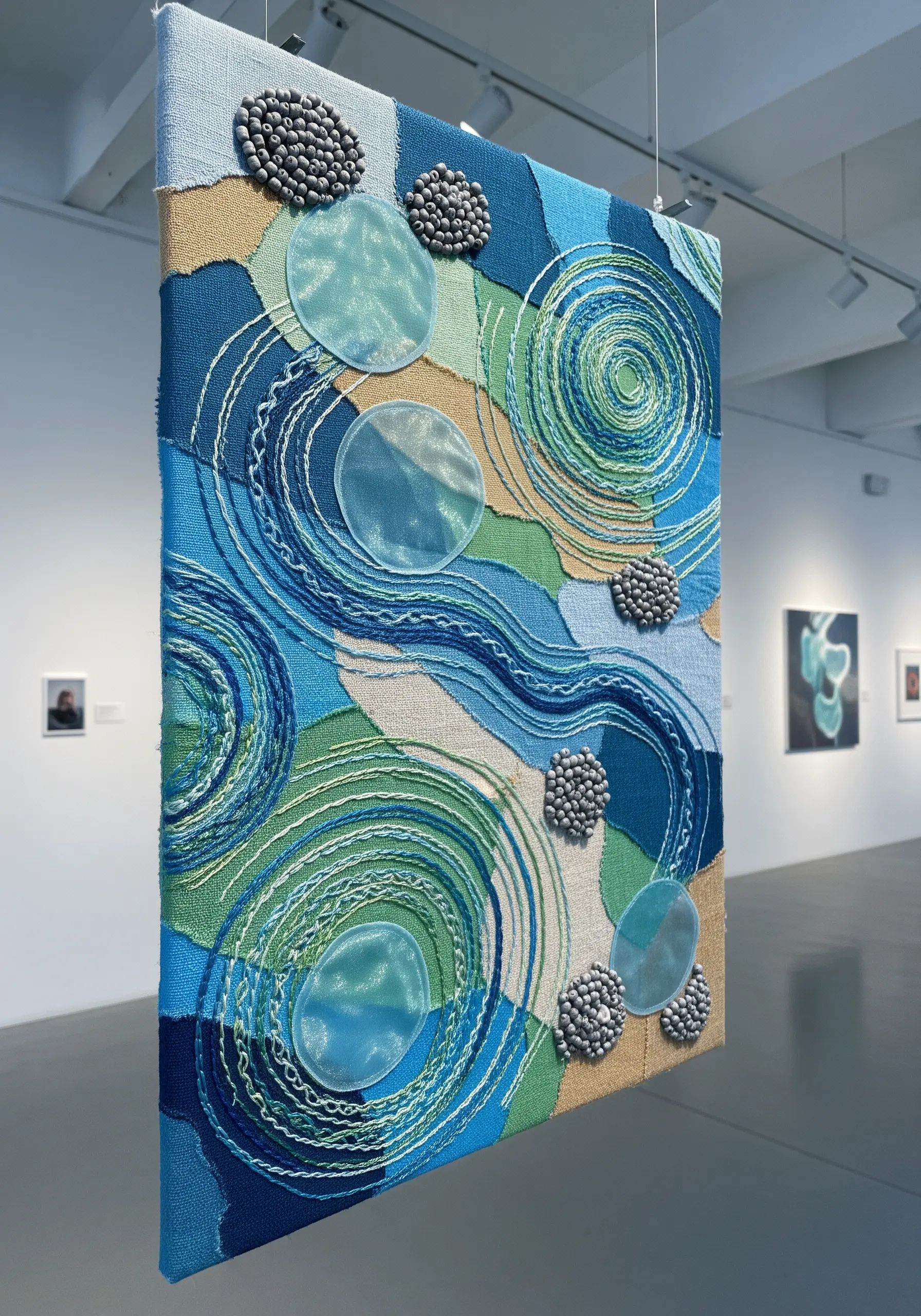 Abstract blue and green fabric collage with sheer circular overlays and swirling stitched lines.