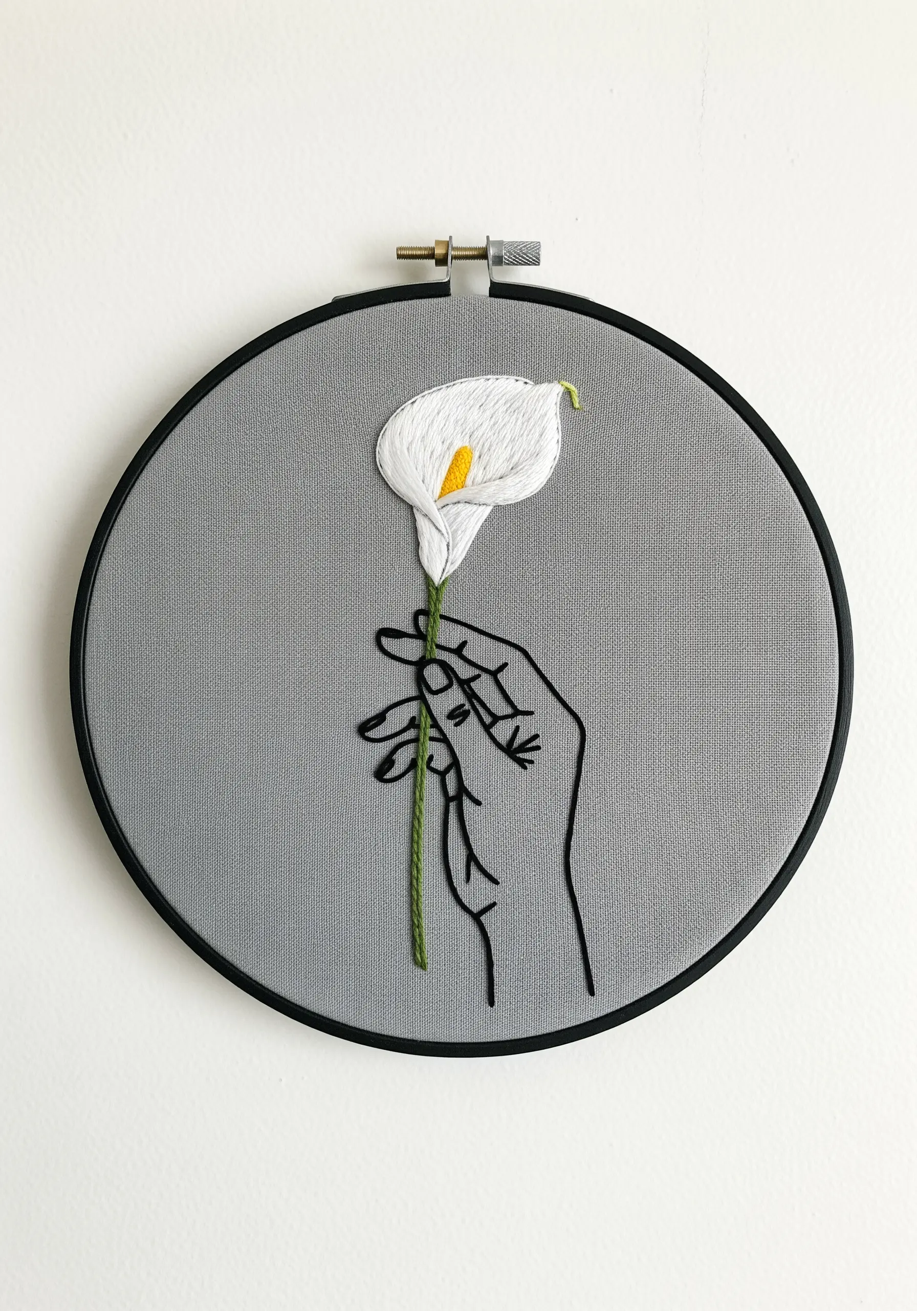 Line art hand holding a white padded satin stitch calla lily on grey fabric.