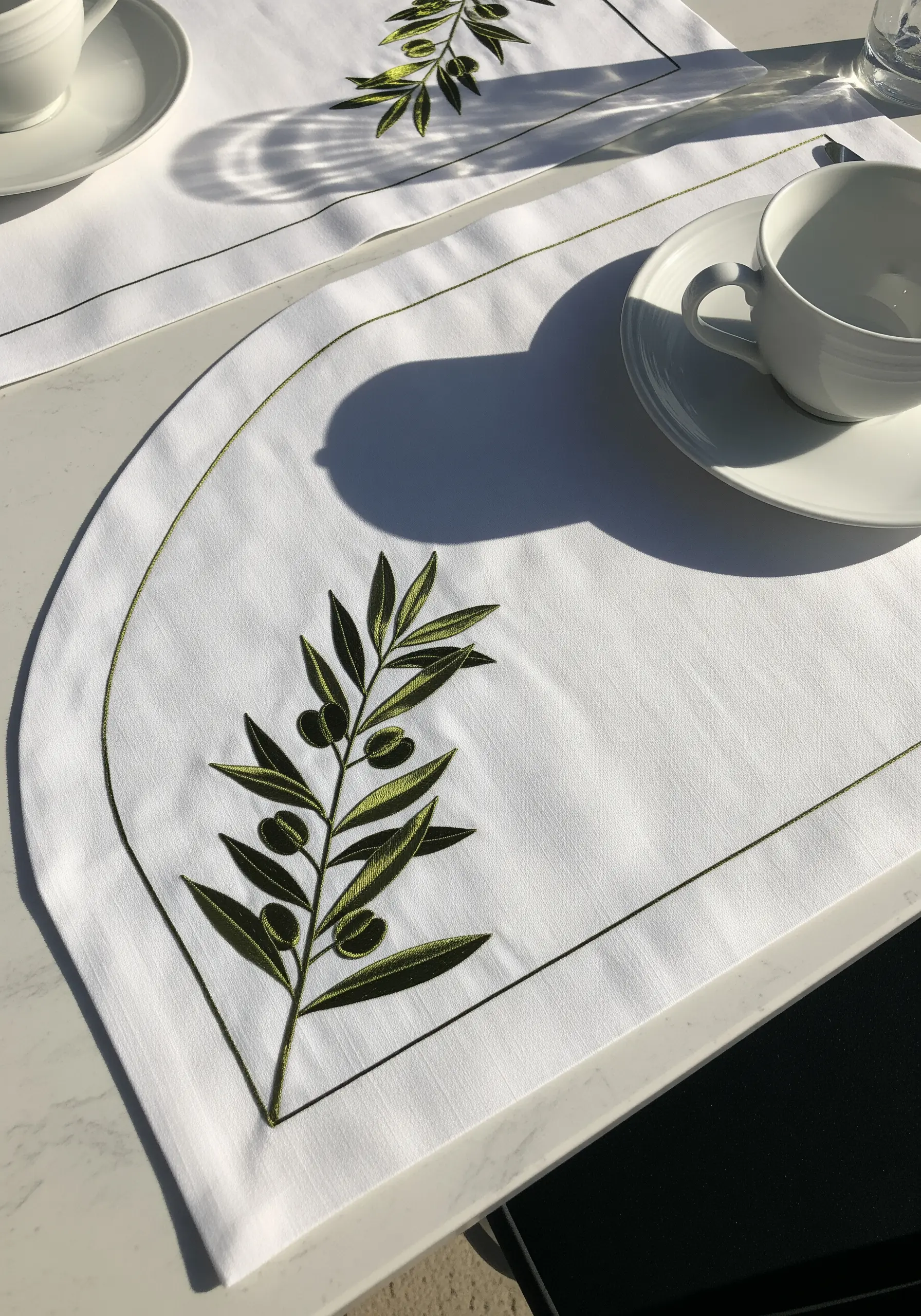 An olive branch with two-tone green leaves and olives embroidered on a white table placemat.