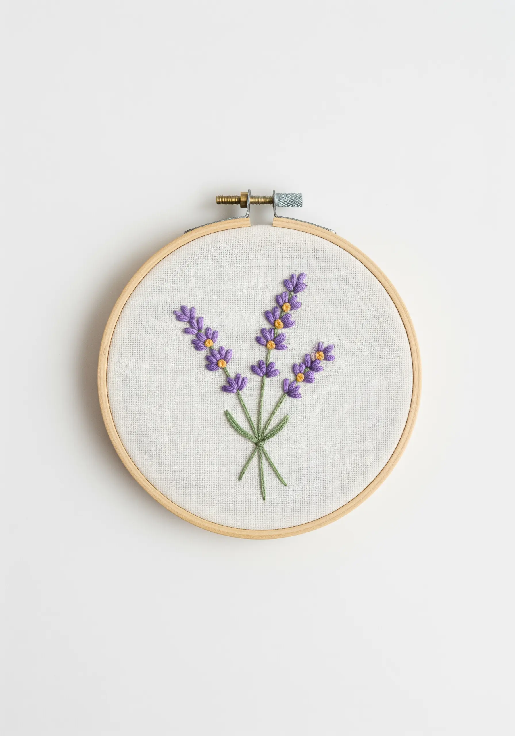 Embroidered lavender sprigs with purple French knots on off-white fabric in a hoop.