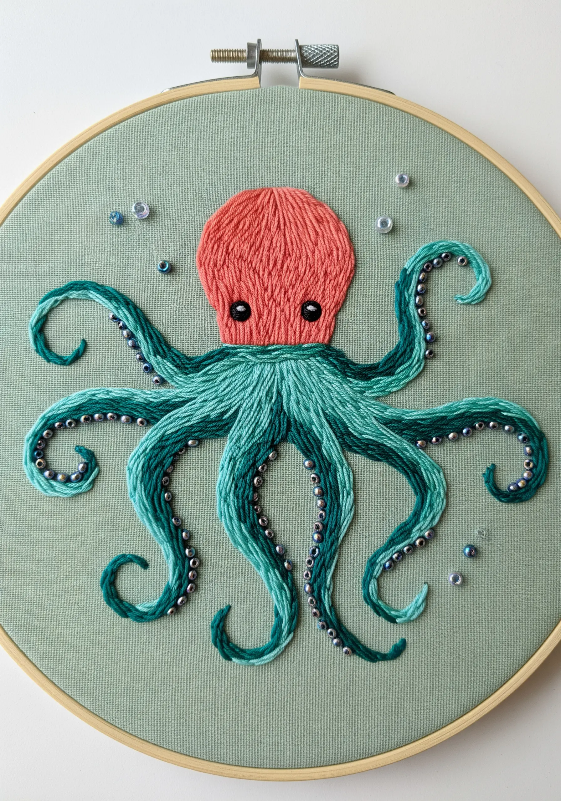 An embroidered octopus with a coral head and textured, beaded tentacles in variegated teal floss.