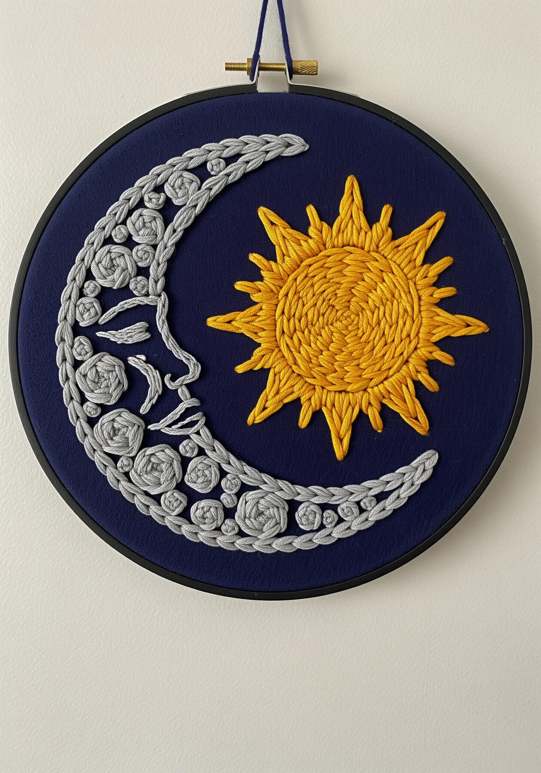 Hoop art with a textured, braided moon and a smooth, spiral-stitched sun motif.