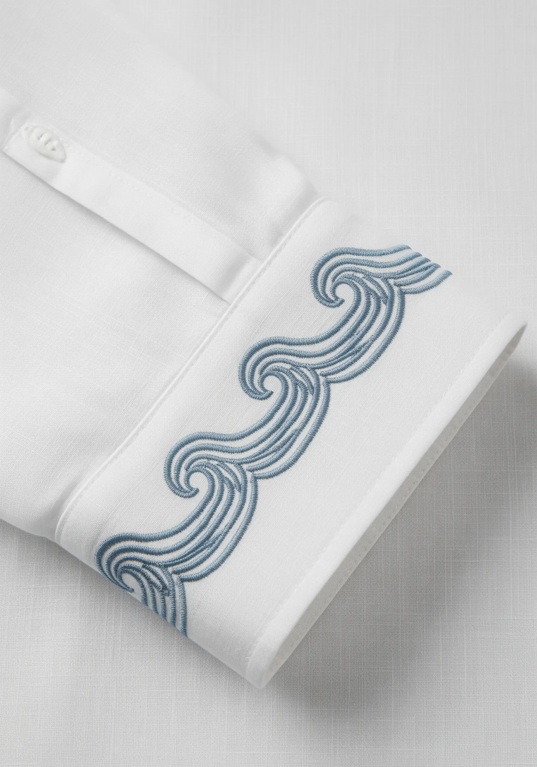 Intricate blue wave pattern embroidered on the white cuff of a dress shirt.