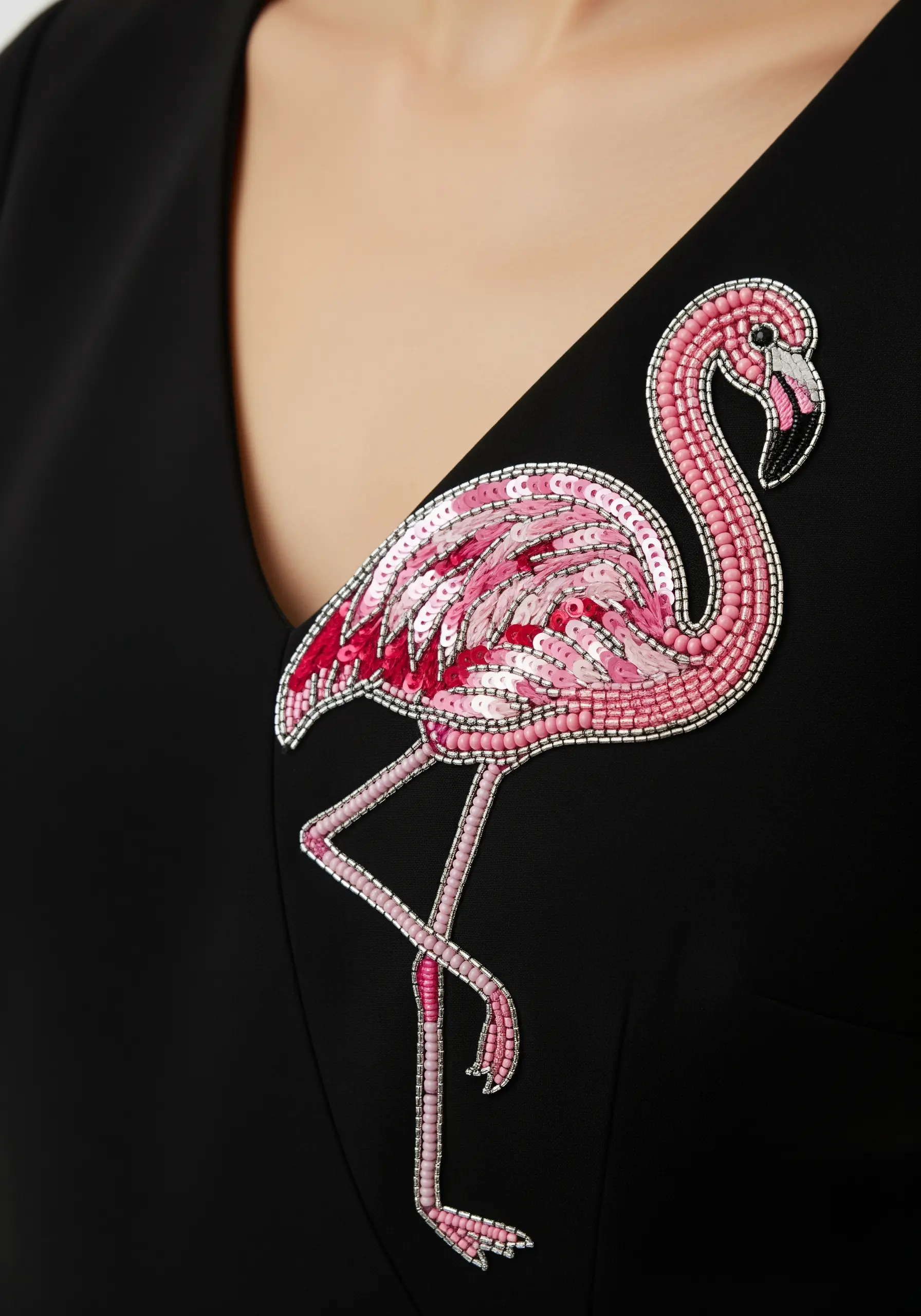 A flamingo brooch made entirely of pink and silver seed beads and sequins on a black dress.