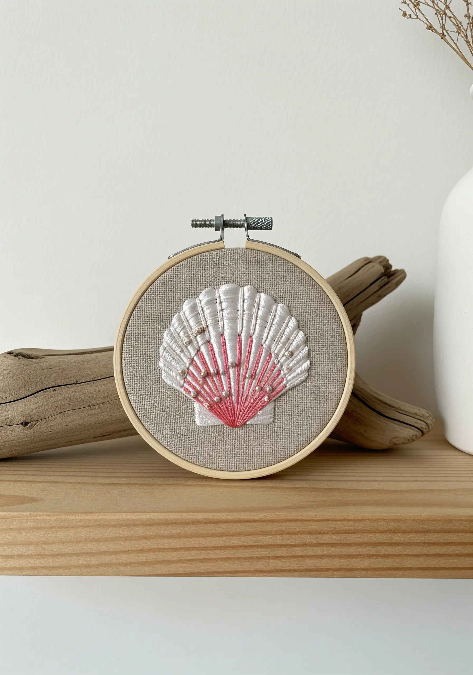 Embroidered seashell with satin stitch and pink beads on neutral linen fabric in a hoop.