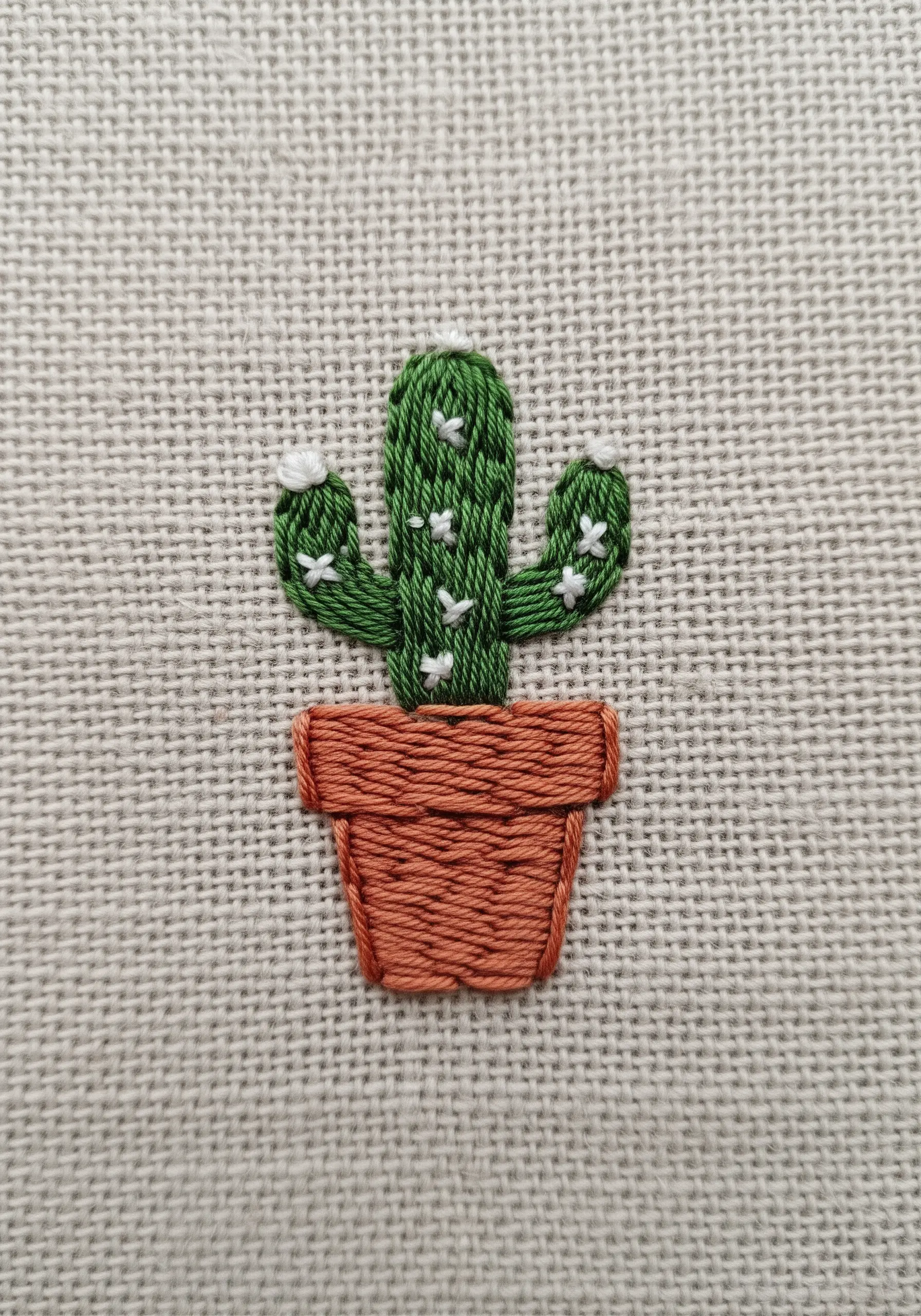 A small embroidered cactus with white seed stitches for spines and a terracotta pot.