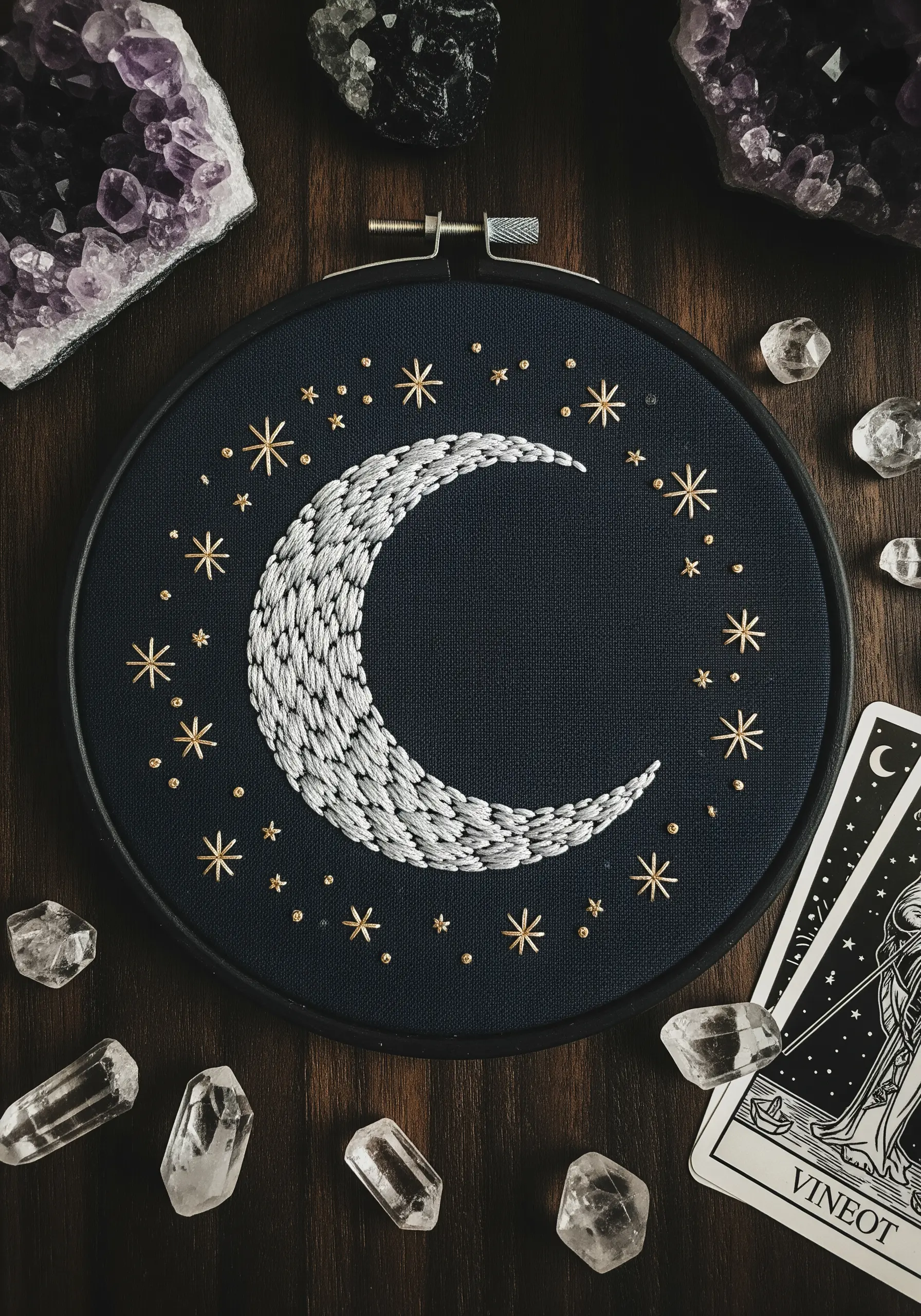 Crescent moon with seed stitch shading, surrounded by gold star stitches on navy fabric.