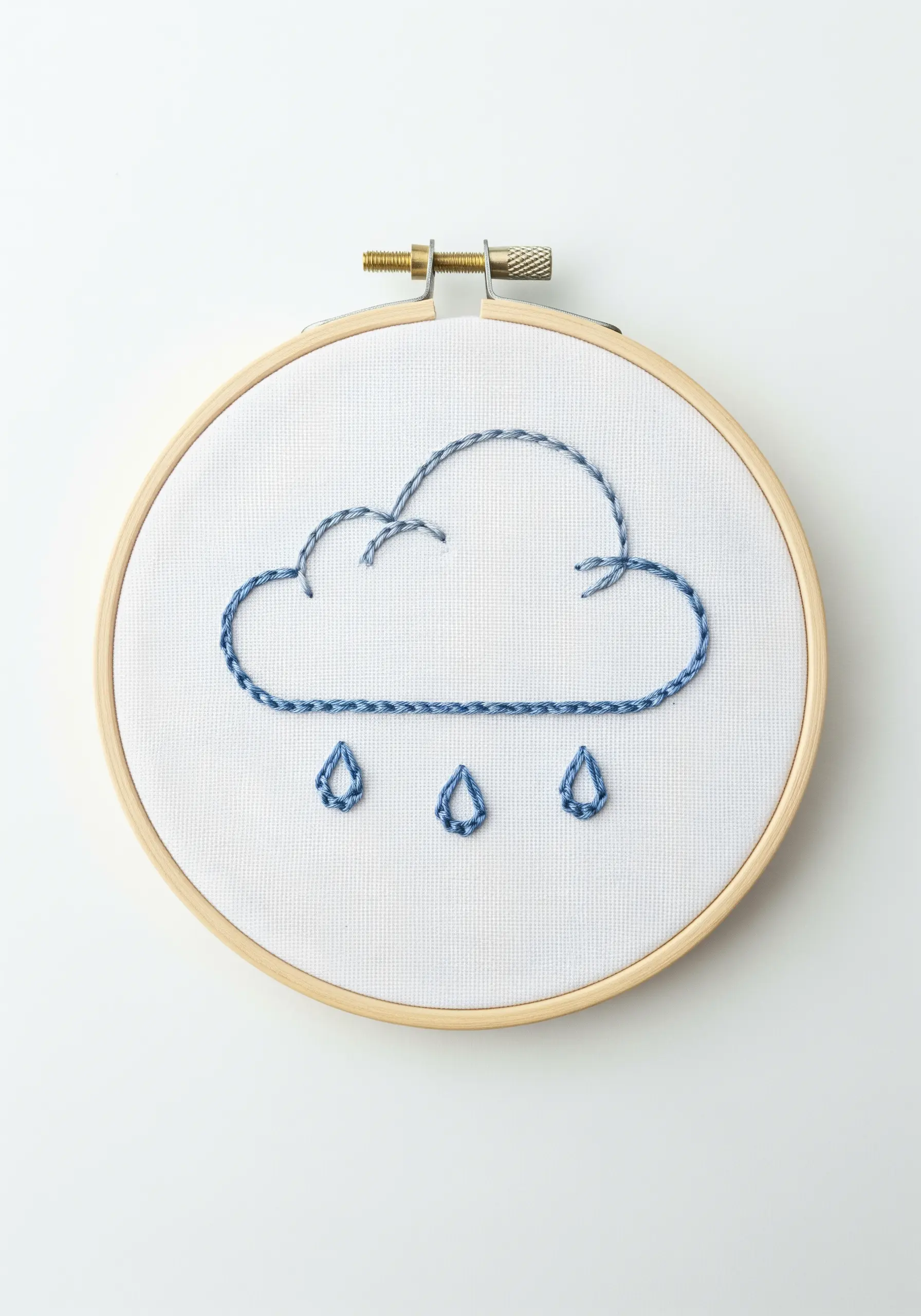 A simple cloud and raindrops outlined in variegated blue thread in a hoop.