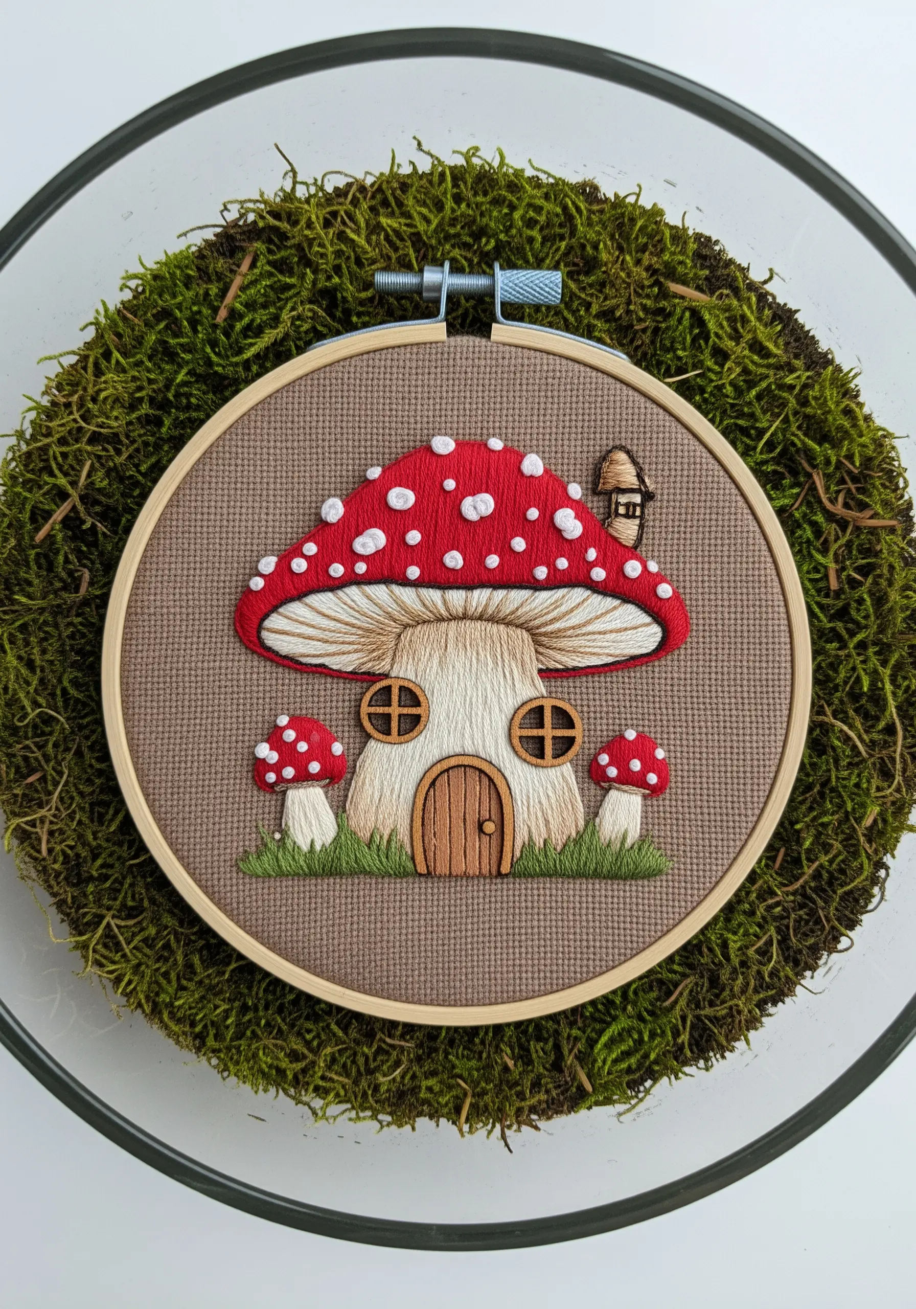 A whimsical mushroom house with a red, polka-dotted roof, embroidered in a terrarium.
