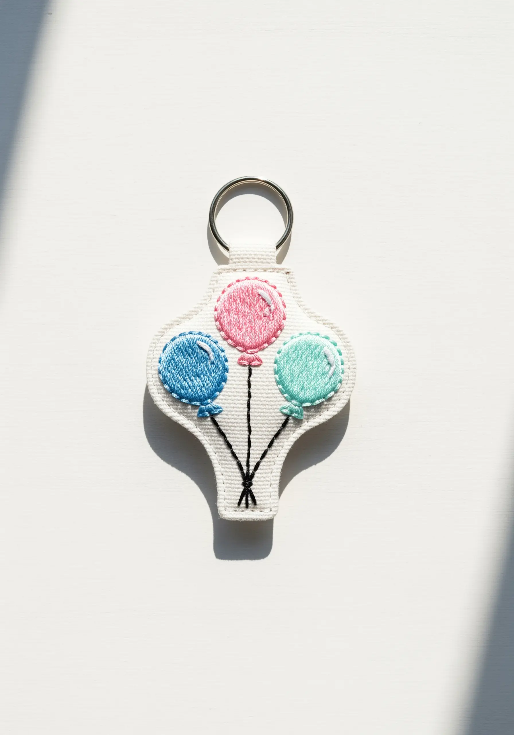 Three pastel embroidered balloons with white thread highlights on a keychain