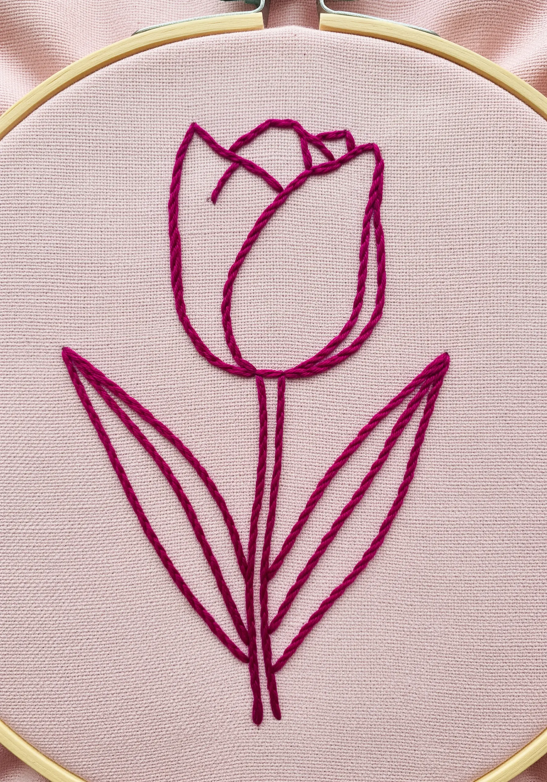 A minimalist tulip outline embroidered in magenta thread using parallel lines of backstitch.