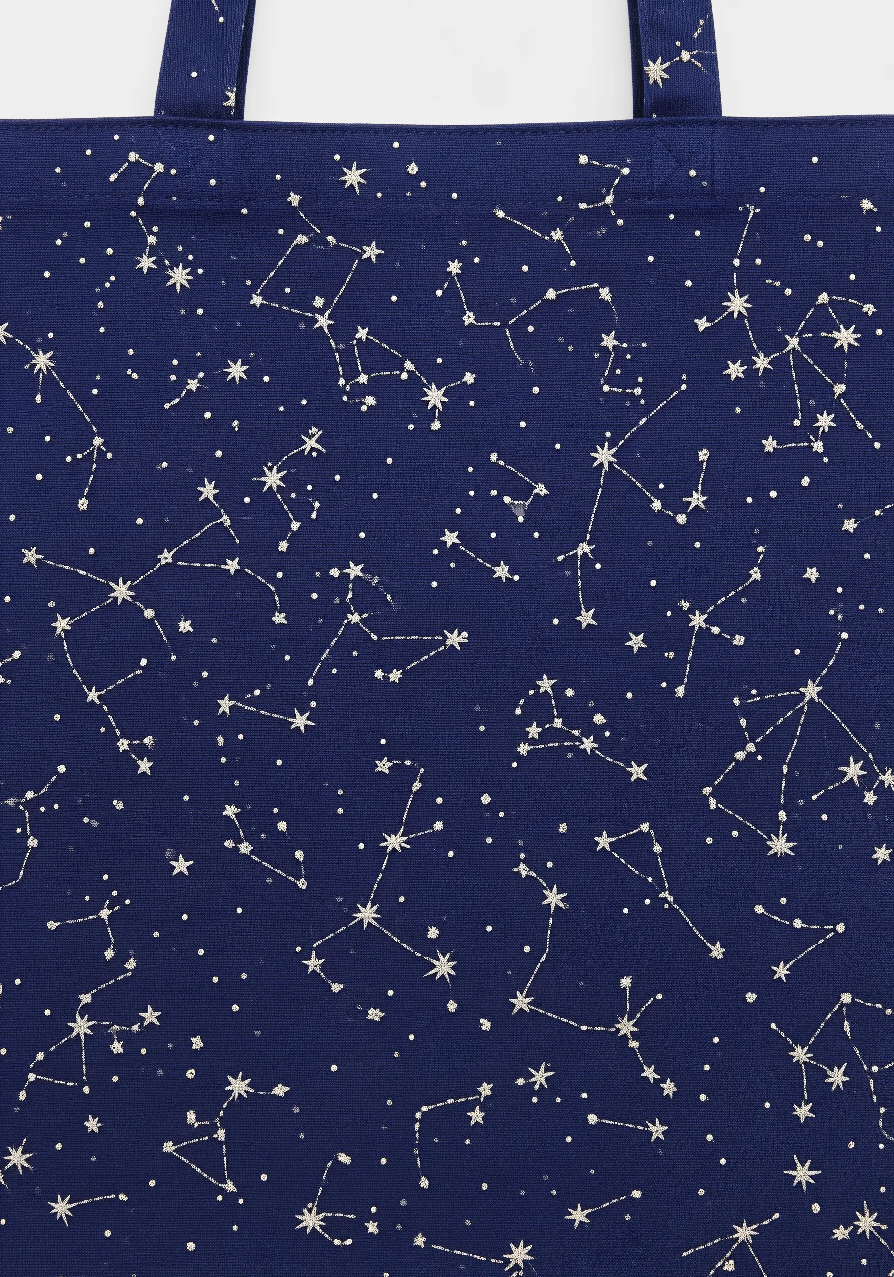 A scattered pattern of white embroidered constellations and stars on a navy blue tote bag.