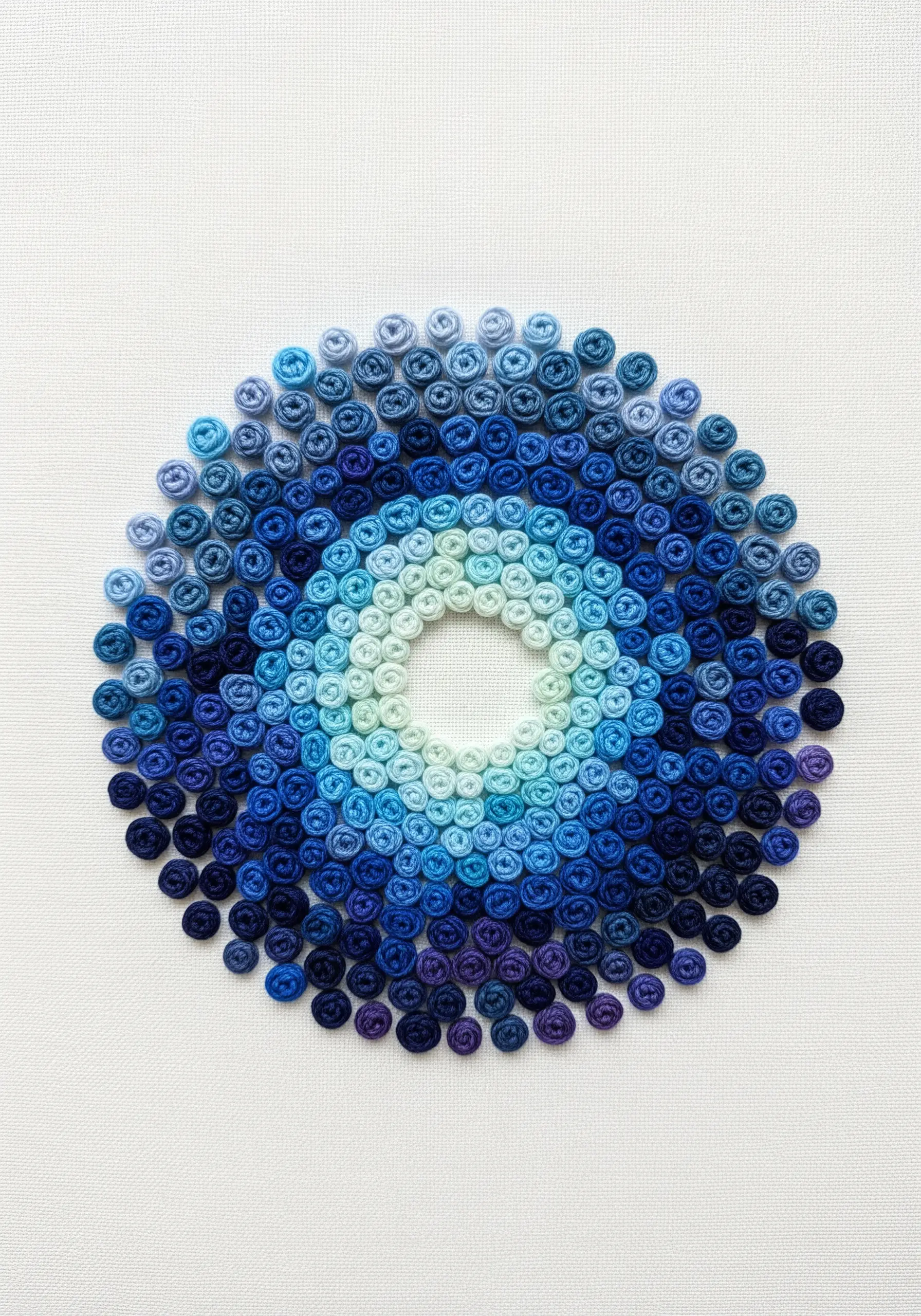A circular gradient of blue woven wheel stitches, from dark to light.