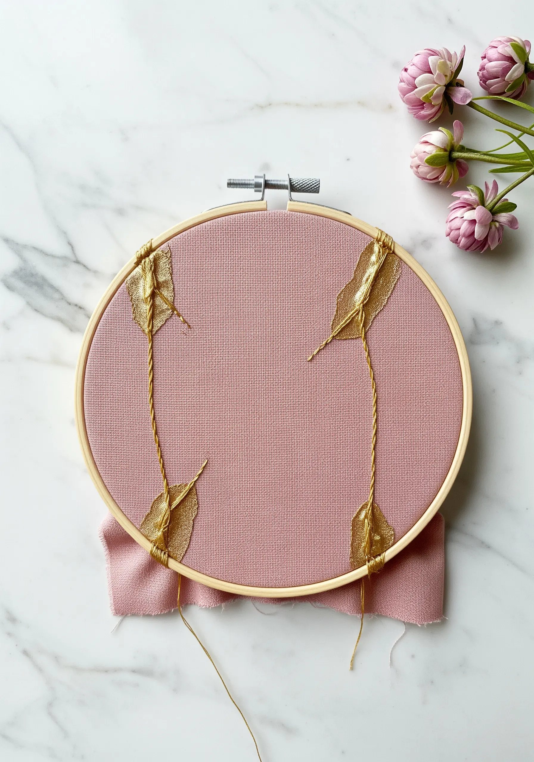 Gold skeleton leaves anchored to pink fabric with wrapped gold thread.