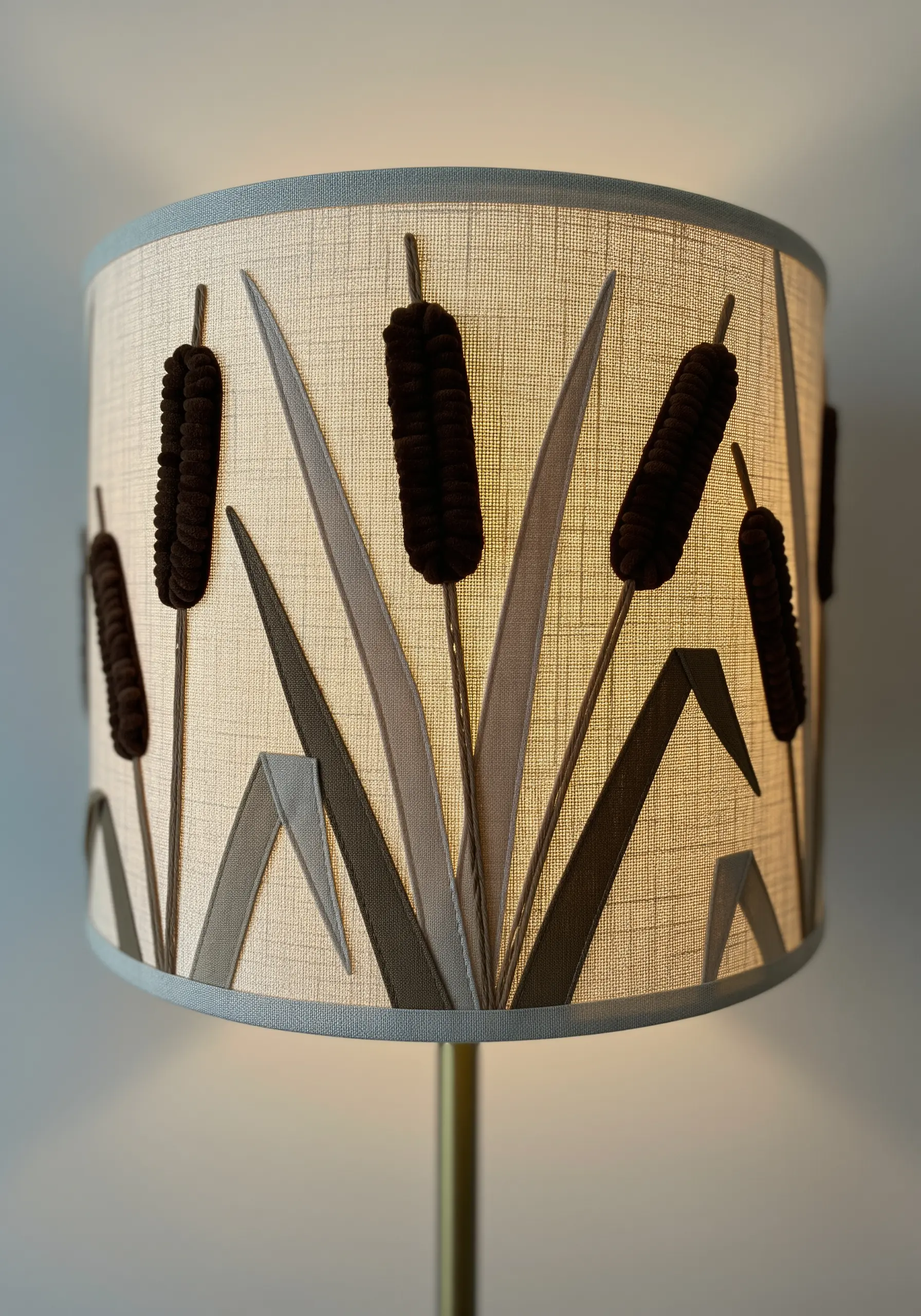 A lampshade decorated with fabric appliqué of cattails, glowing warmly from within.