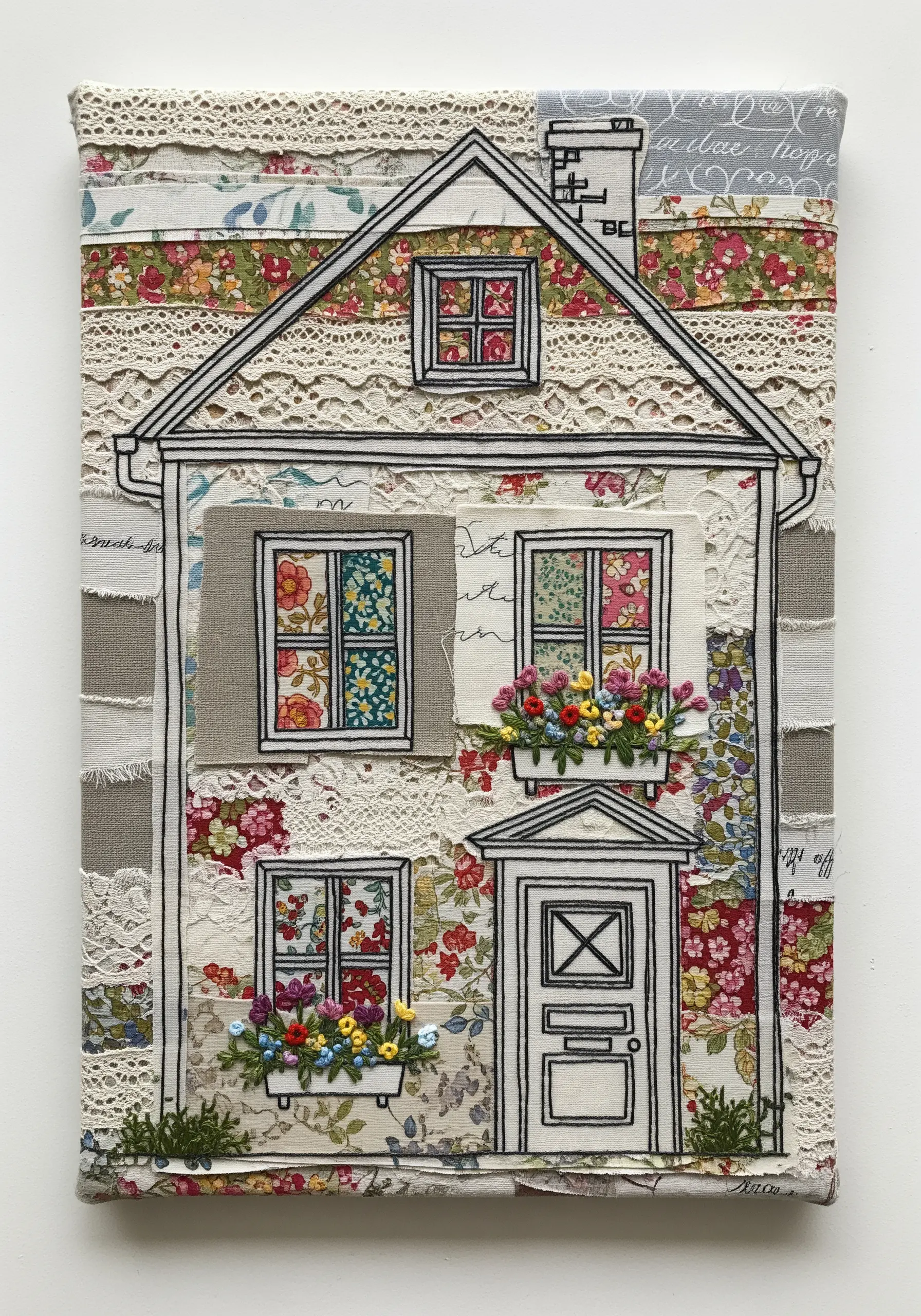 Fabric collage of a house with black thread outlines and embroidered flowers.