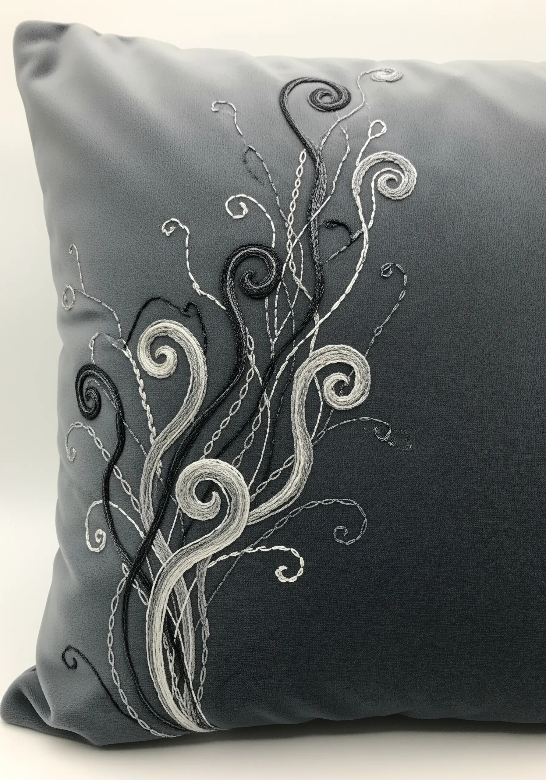 Abstract black, white, and grey swirls embroidered on a grey gradient cushion.