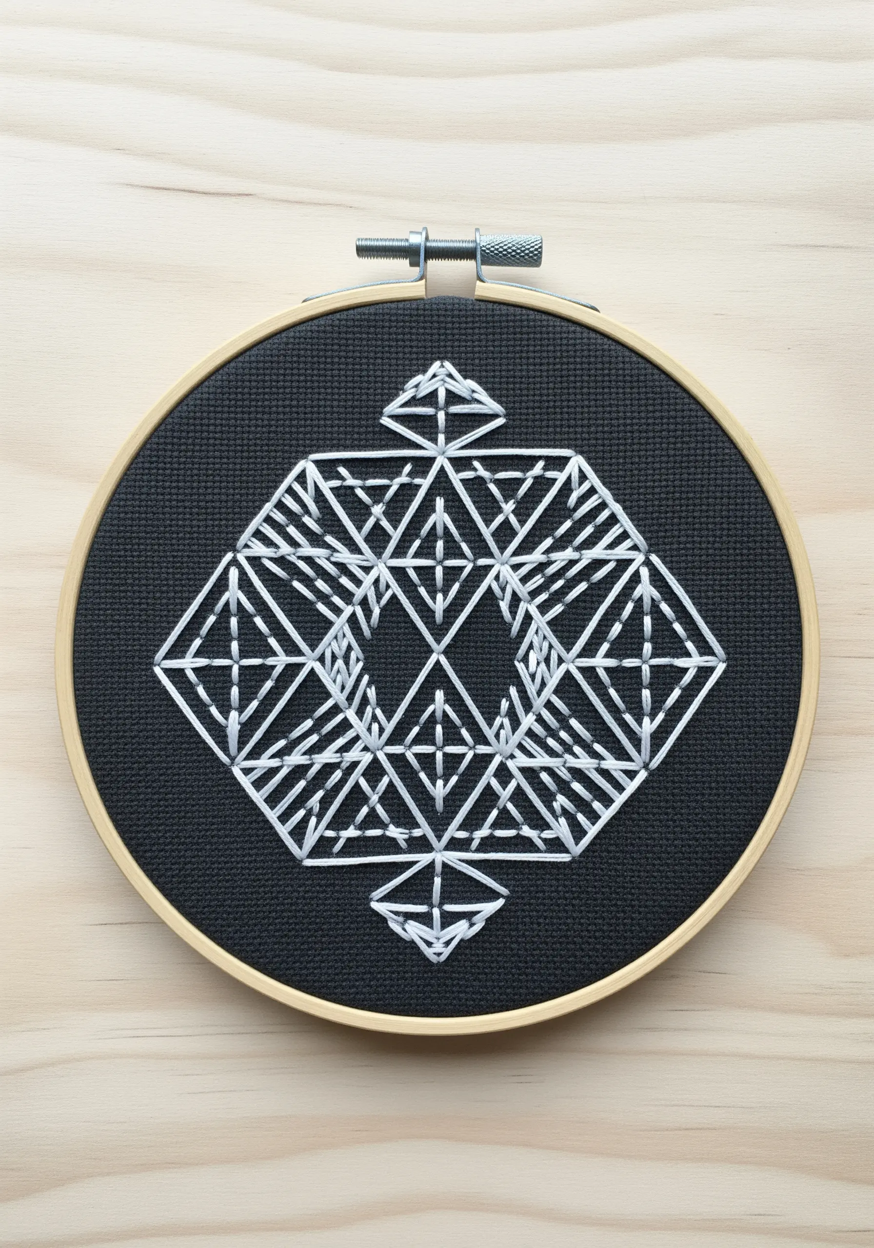 A complex geometric 3D shape stitched in white thread on black Aida cloth.