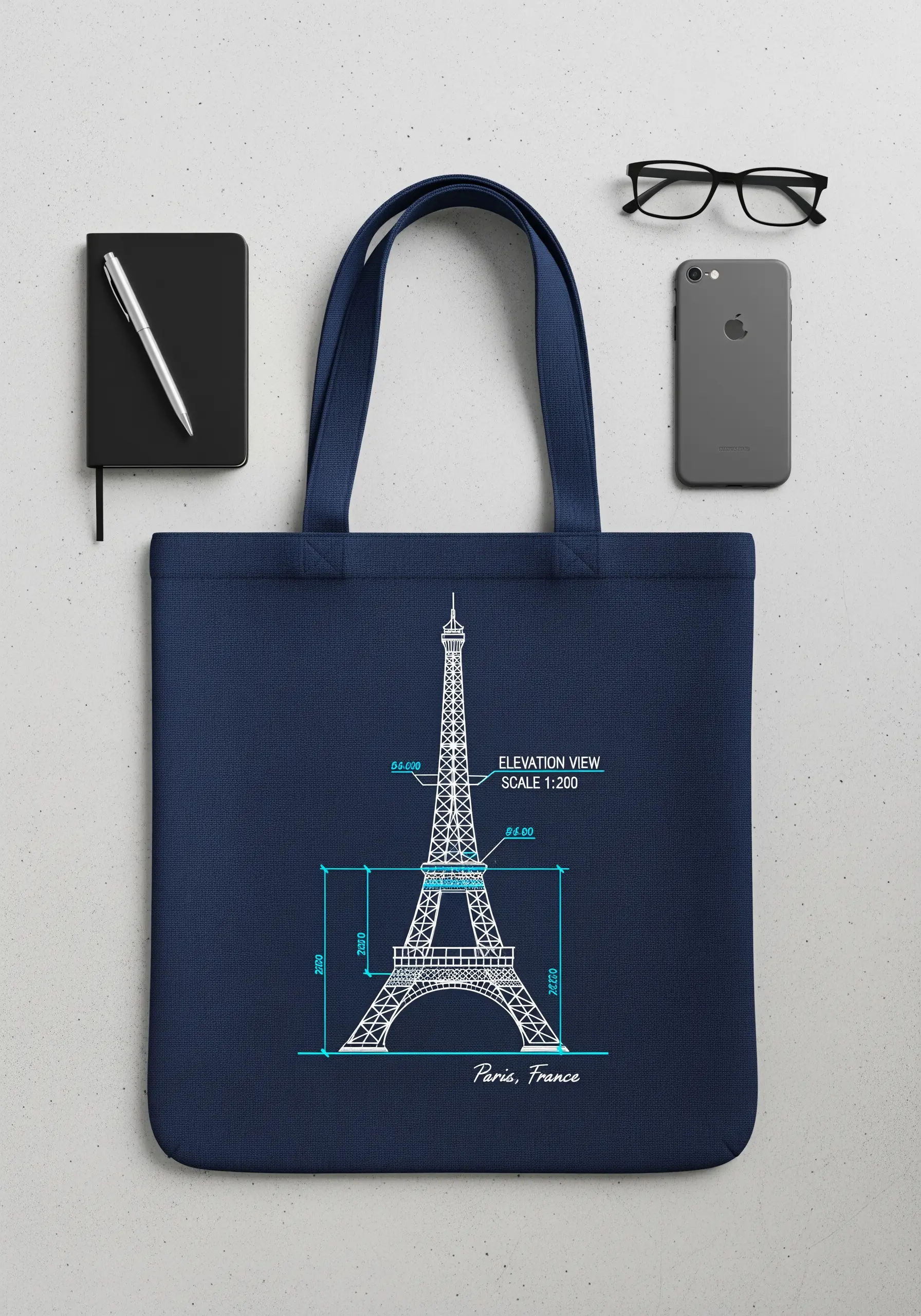 An architectural blueprint of the Eiffel Tower embroidered in white thread on a navy blue tote bag.