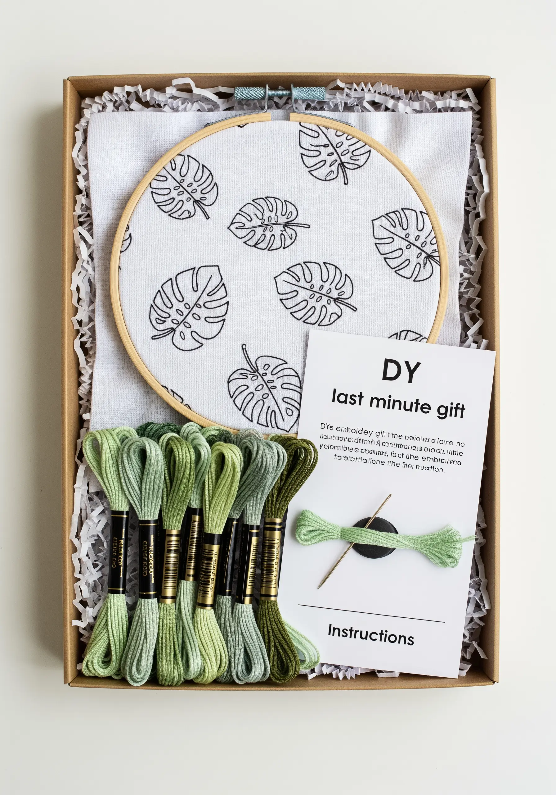 A DIY embroidery kit in a box with monstera-printed fabric, green threads, a hoop, and instructions.