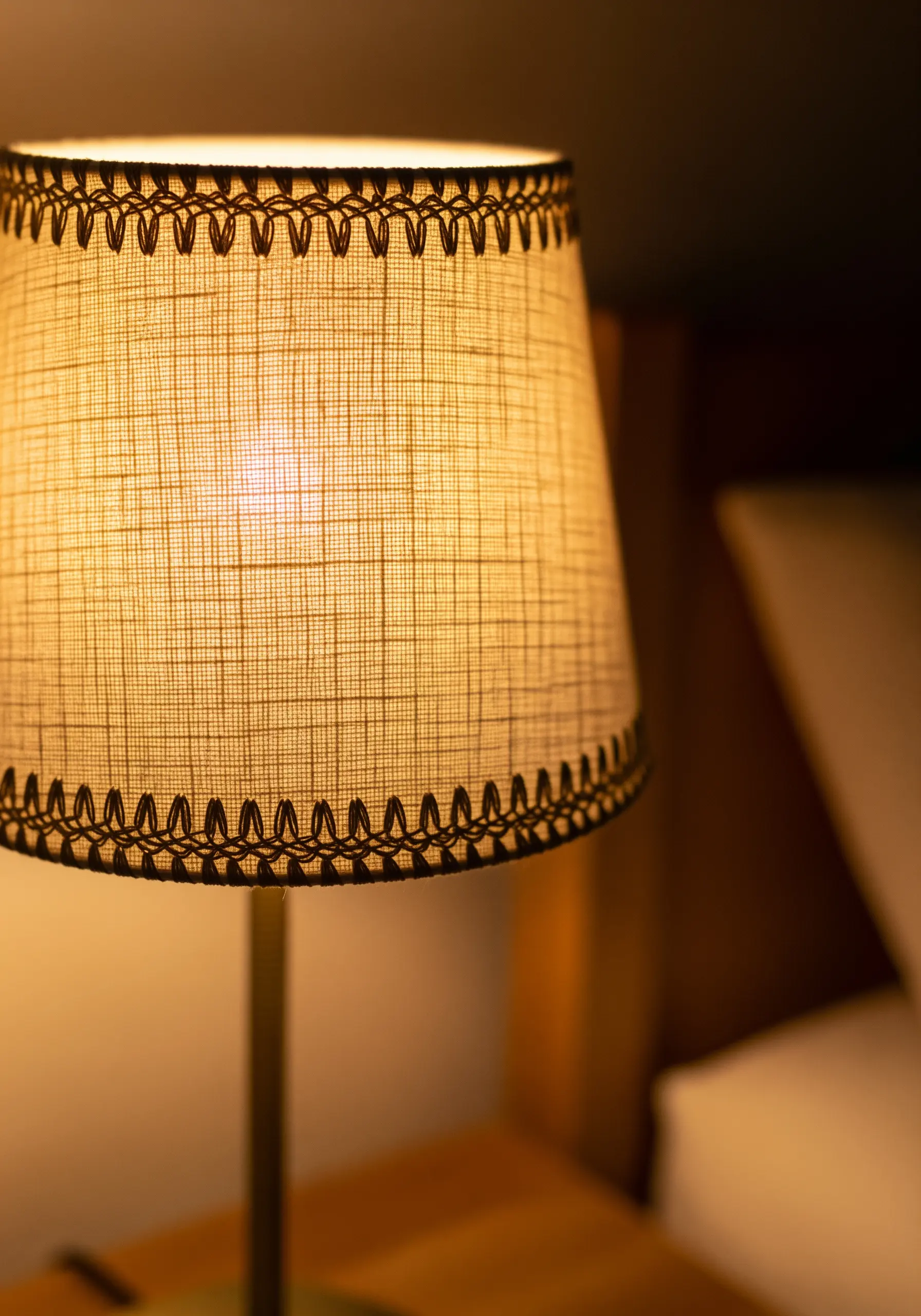 Close up of a lit lamp shade with a decorative dark brown embroidery stitch along the bottom rim