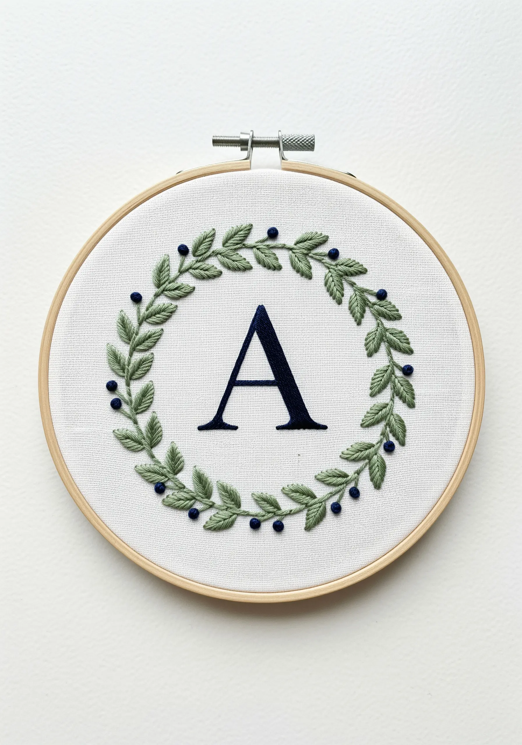 An embroidered letter 'A' inside a green leafy wreath with blue berry details.